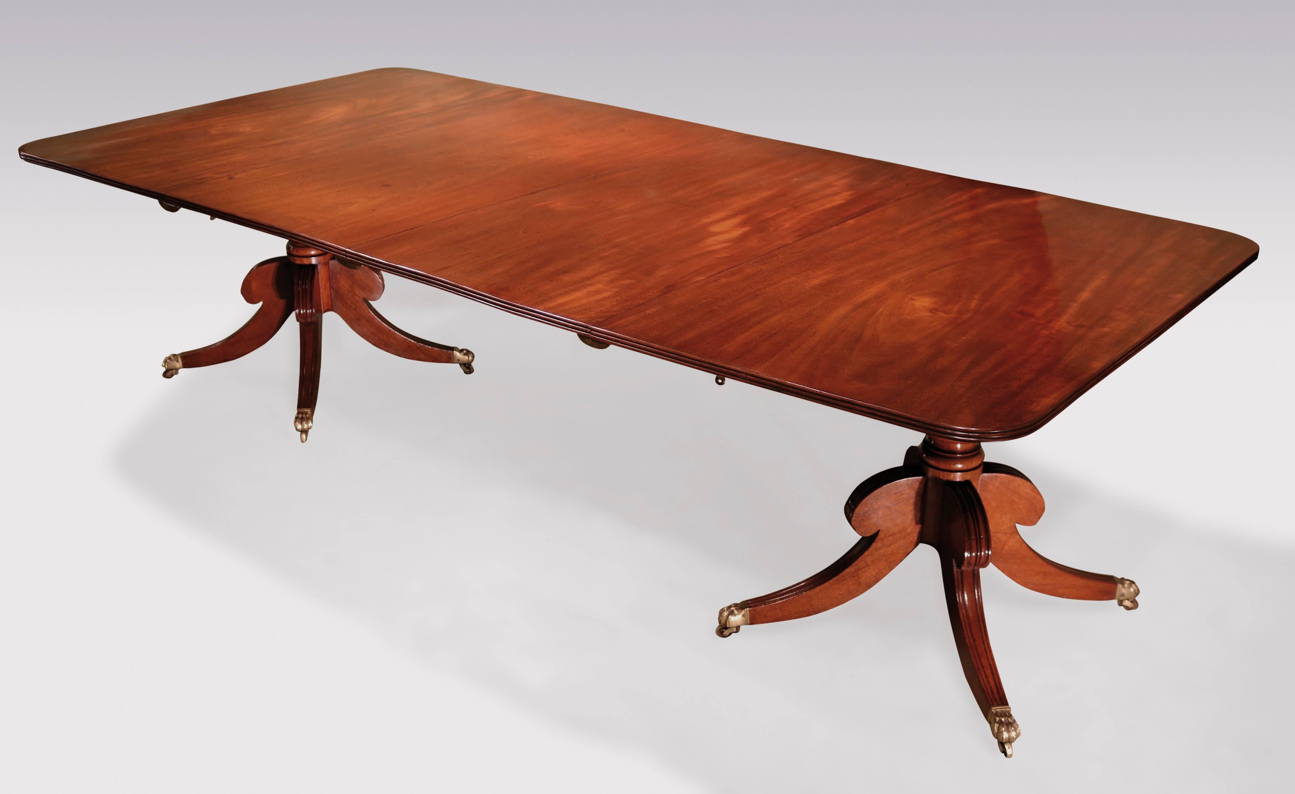 An early 19th century Regency period well-figured mahogany two-pedestal dining table fitted with two leaves, having reeded edged tops, supported on ring-turned stems above reeded four-splay legs ending on original lion’s paw brass castors. Measures: