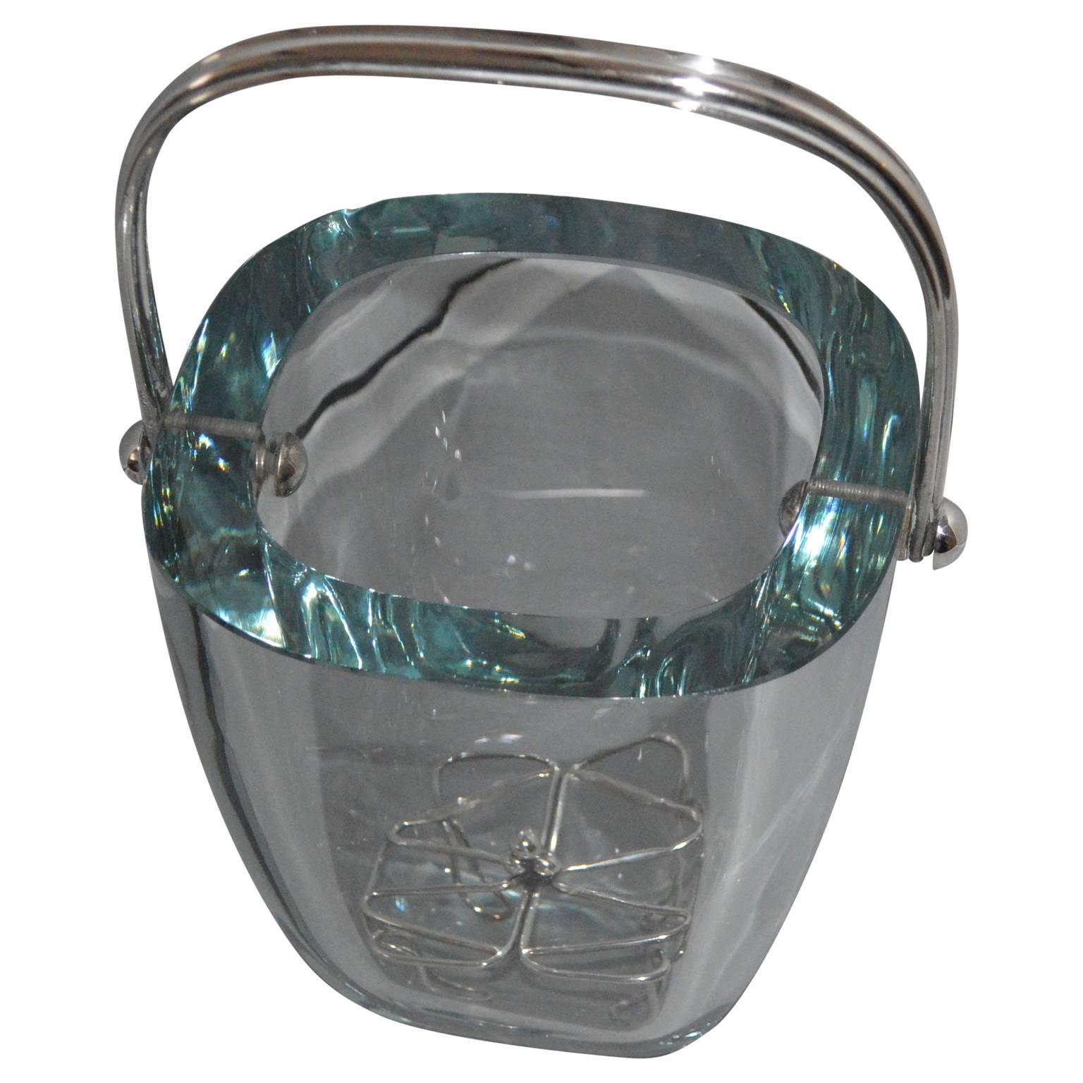 Glass and sterling silver ice bucket and stand by Strombergshyttan, Sweden, 1970s.
Transparent aqua blue tinted thick glass vessel, mounted with sterling silver handle, from Strombergshyttan (maker). Handle and ice cube stand is made in sterling