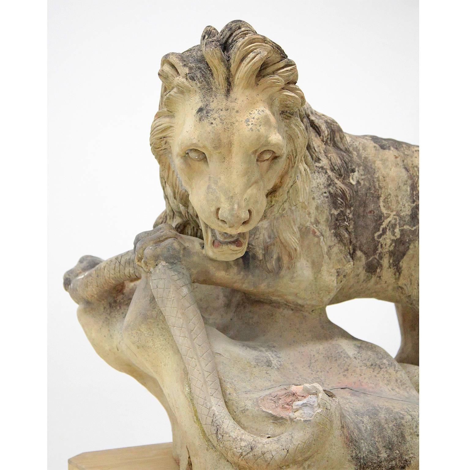 Naturalistic and complementary designed sculptures of lions on landscape bases with open mouths in a tense and belligerent posture. The lion has just caught a snake and is about to fight it, while the lioness has a suckling pup underneath her. The