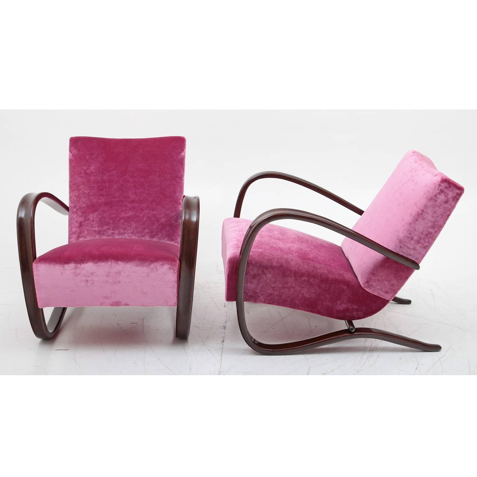 Iconic pair of chairs from the famous Czech designer Jindrich Halabala. The dark-stained armrests flow in an elegant c-shape around the side of the seating surface and become the frame of the chair. The chairs have been reupholstered.
