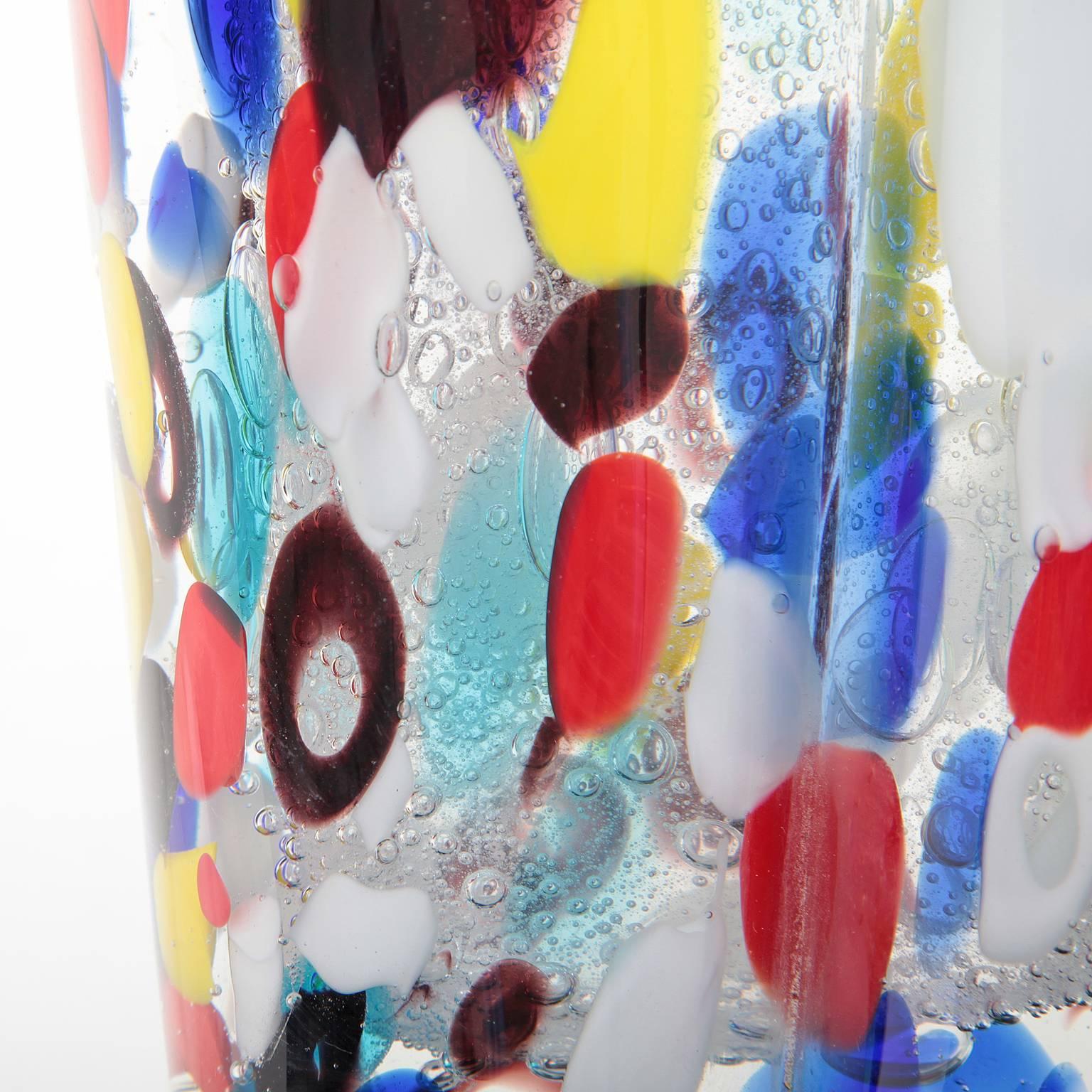 A glass sculpture on a round base in the form of a female torso. The piece is streaked with colorful dots in the typical manner.