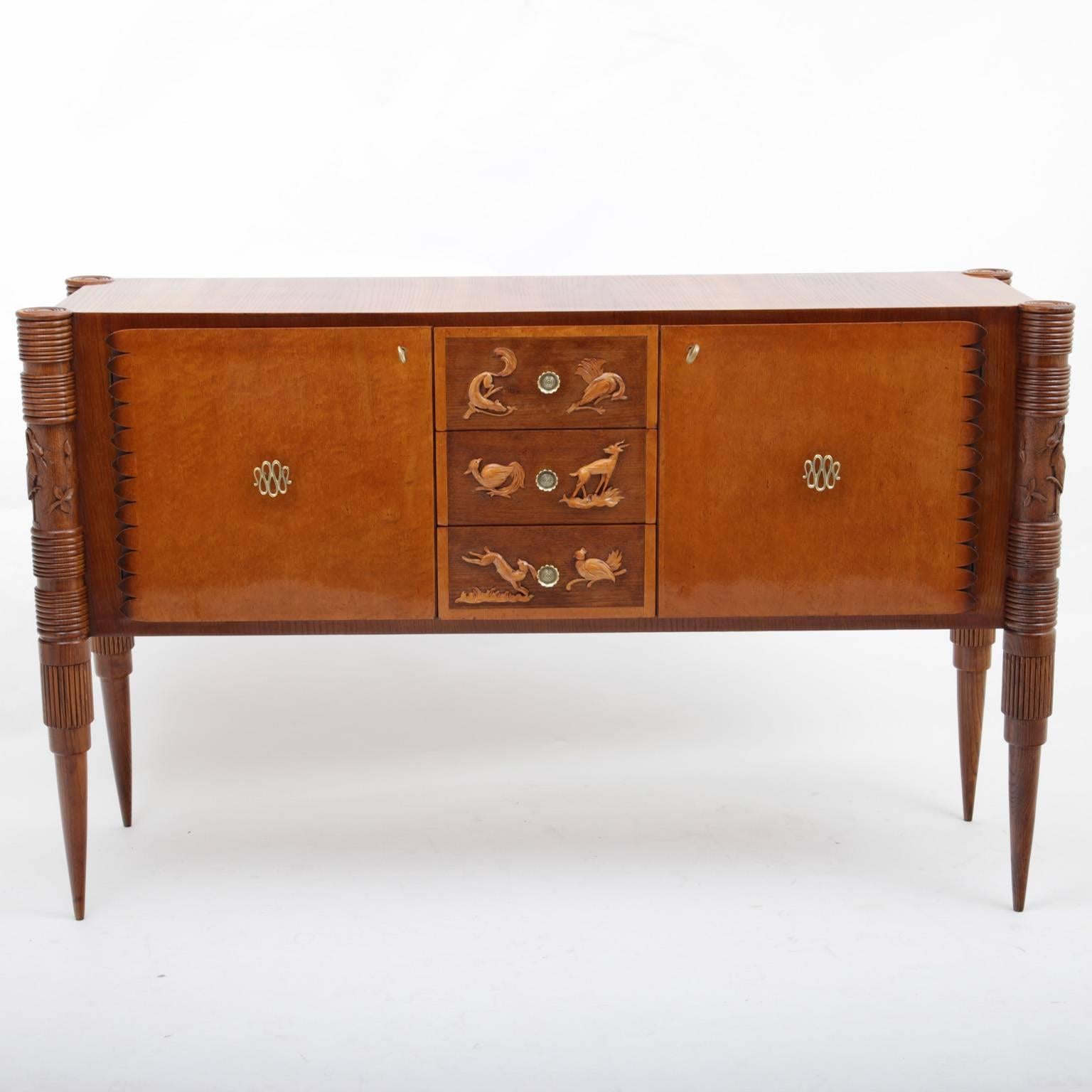Sideboard by the Italian designer Pier Luigi Colli on conical legs with two doors and three drawers. Unusual carved legs with grooves and carved crane and leaves motives. The brass handles are in the shape of a wound snake. Fine animal carvings