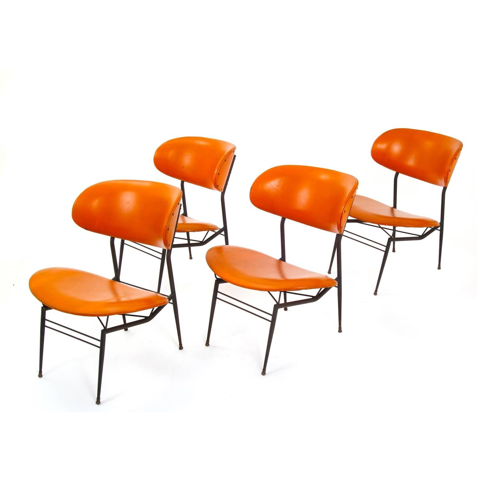Four leather chairs in the style of Gastone Rinaldi for RIMA, on black metal frames with oval seats and backrests which are covered with orange leather.