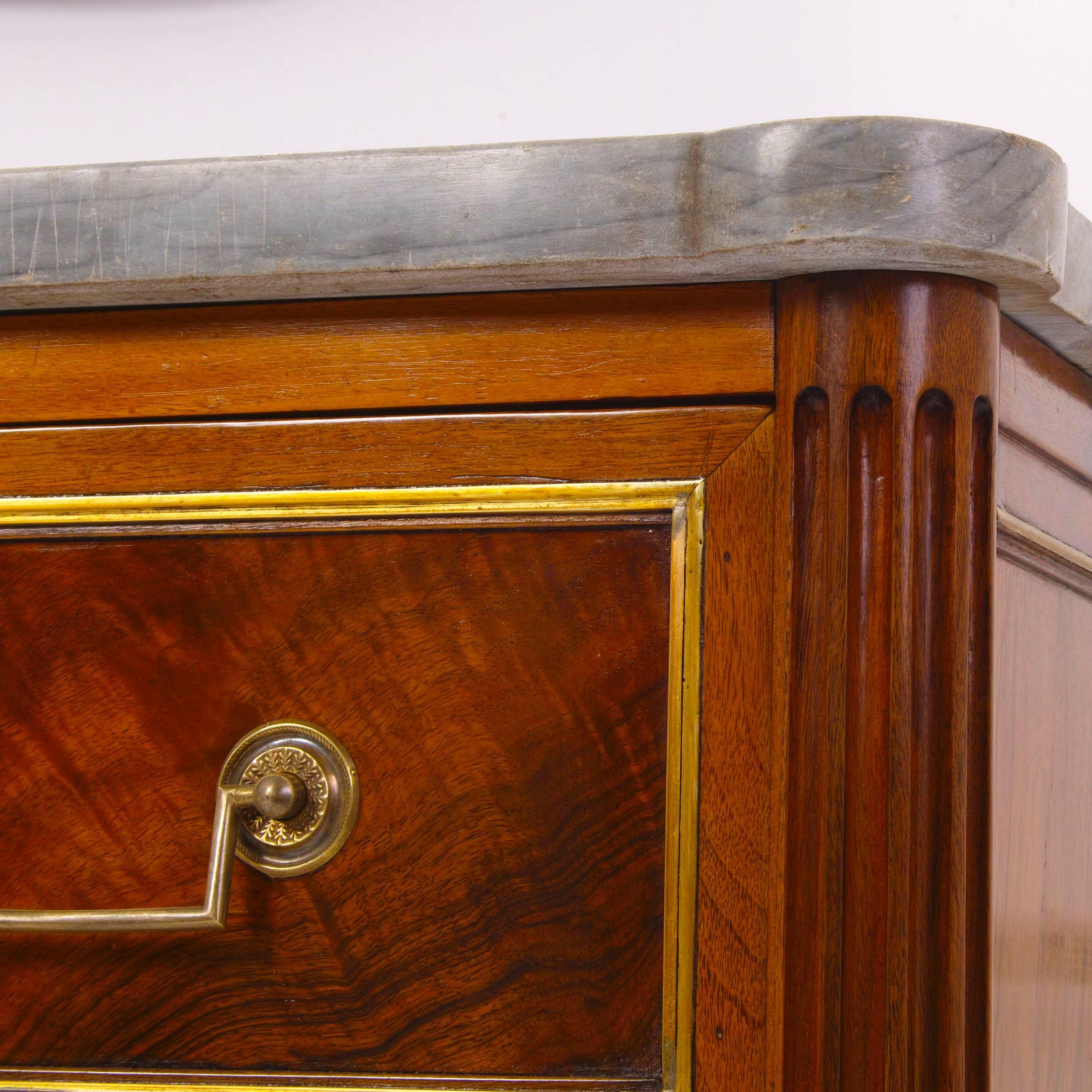 Three-drawered chest on cone legs with fluted column-shaped corners and bronze handles and escutcheons. The tabletop is grey marble. The chest is in original condition, the French polish is restored.