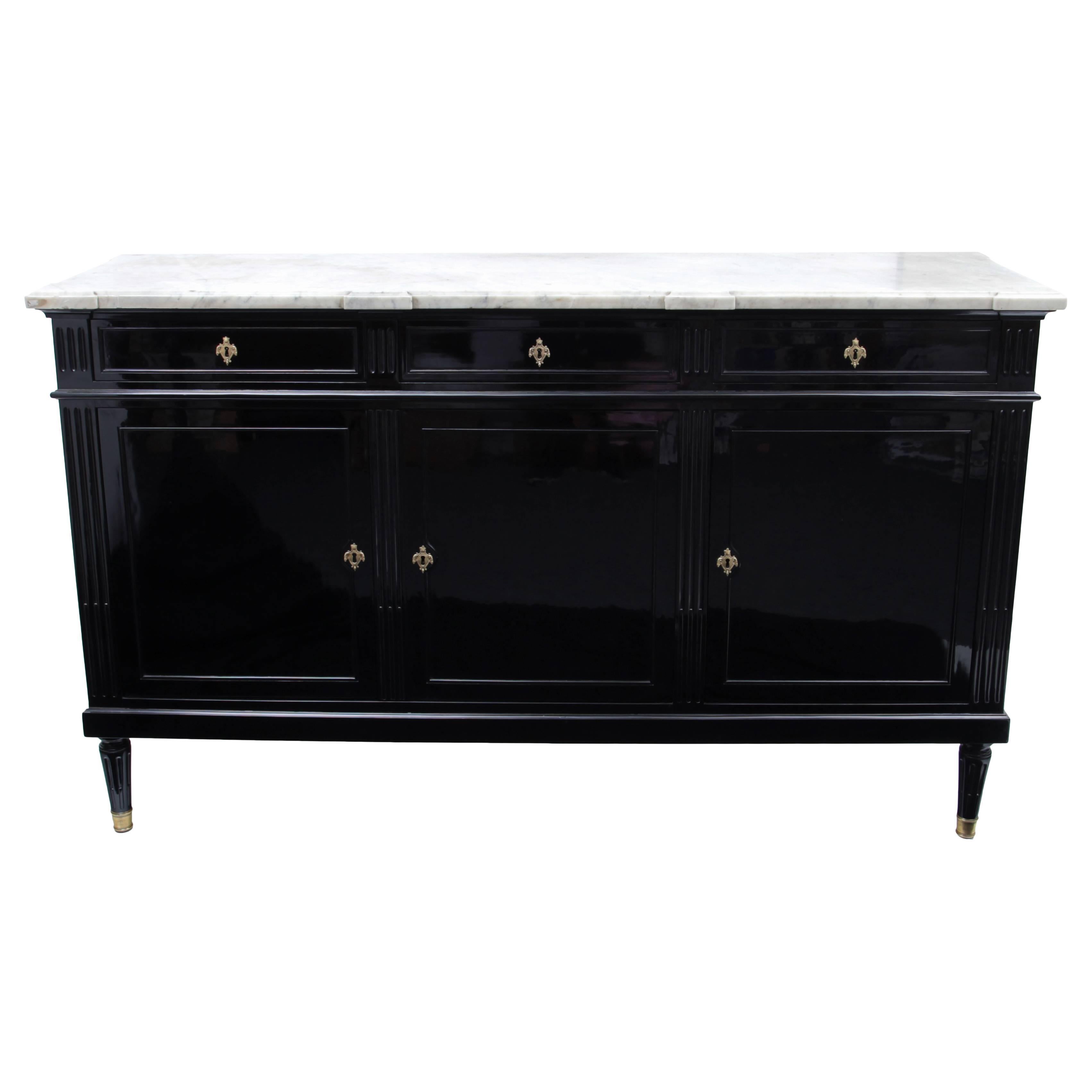Completely ebonized sideboard with white marble top. The corpus has three doors and three top drawers with bronze escutcheons. The corners are in the shape of pilasters with fluted shafts. The legs are baluster-shaped and have bronze caps.