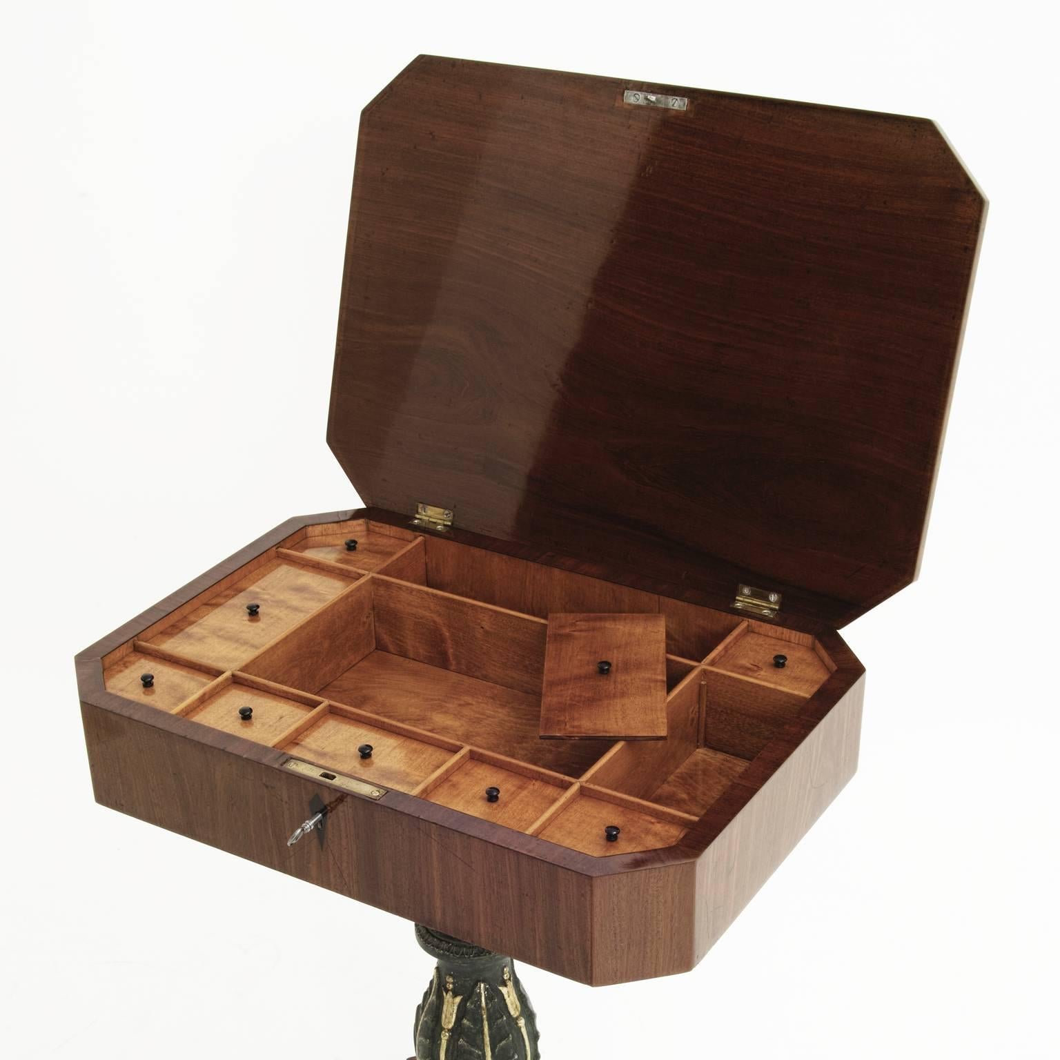 Mahogany sewing table on lion’s feet on a quatrefoil stand and a green and gilt middle column. The octagonal tabletop has several compartments on the inside.
                 