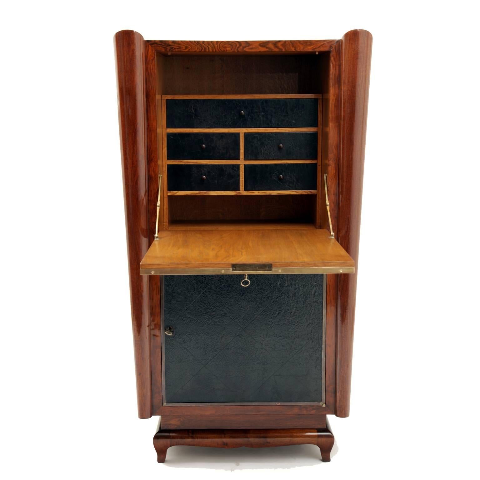 Slim Art Deco secretaire with trapezoidal corpus on low feet. The front is decorated with leather and framed with brass bars. The interior has two compartments and five drawers, also decorated with a textured leather. The lower cabinet has one shelf.