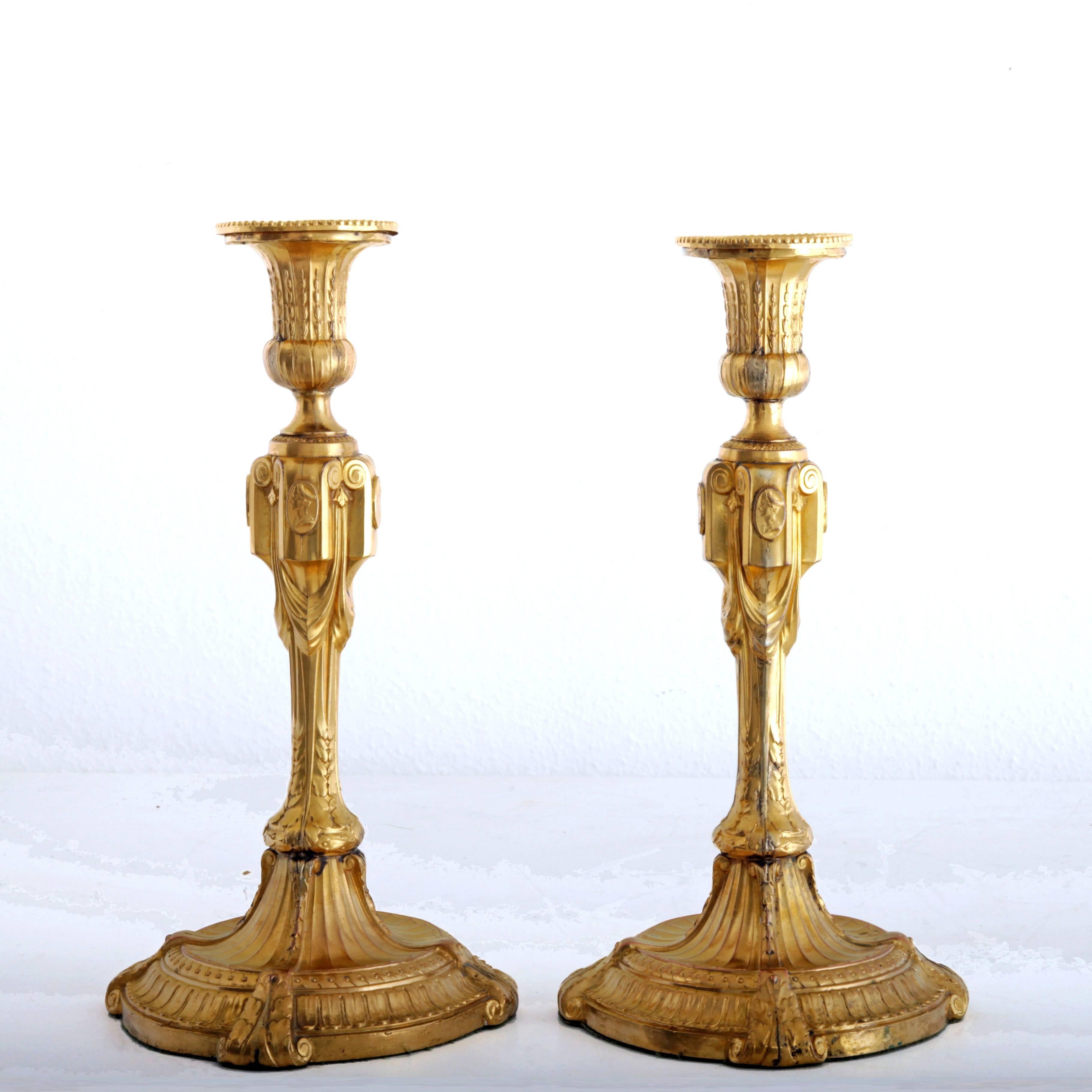 Pair of gilt metal candlesticks with neoclassical decor and scrolls. The shaft is decorated with cameos.