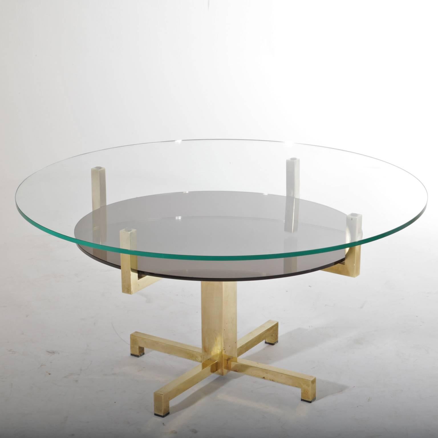 Coffee table with round glass tabletop on a x-shaped brass base. The lower shelf is smoked glass.