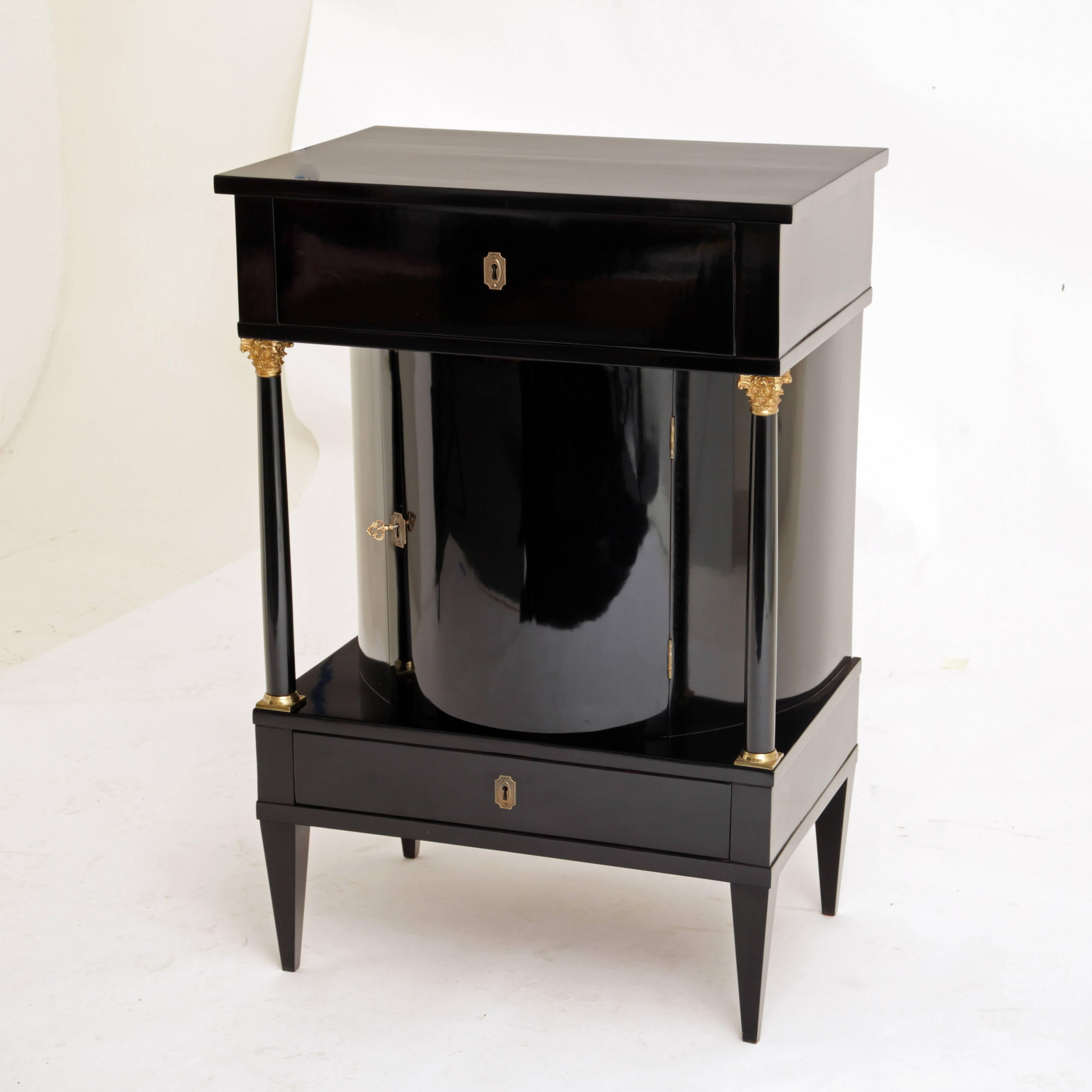 Ebonized cabinet on tapered feet with two drawers and a rounded middle compartment, flanked with columns with gilded capitals and bases. The top drawer has a foldable writing shelf and an extendable lateral compartment. The cabinet is perfectly