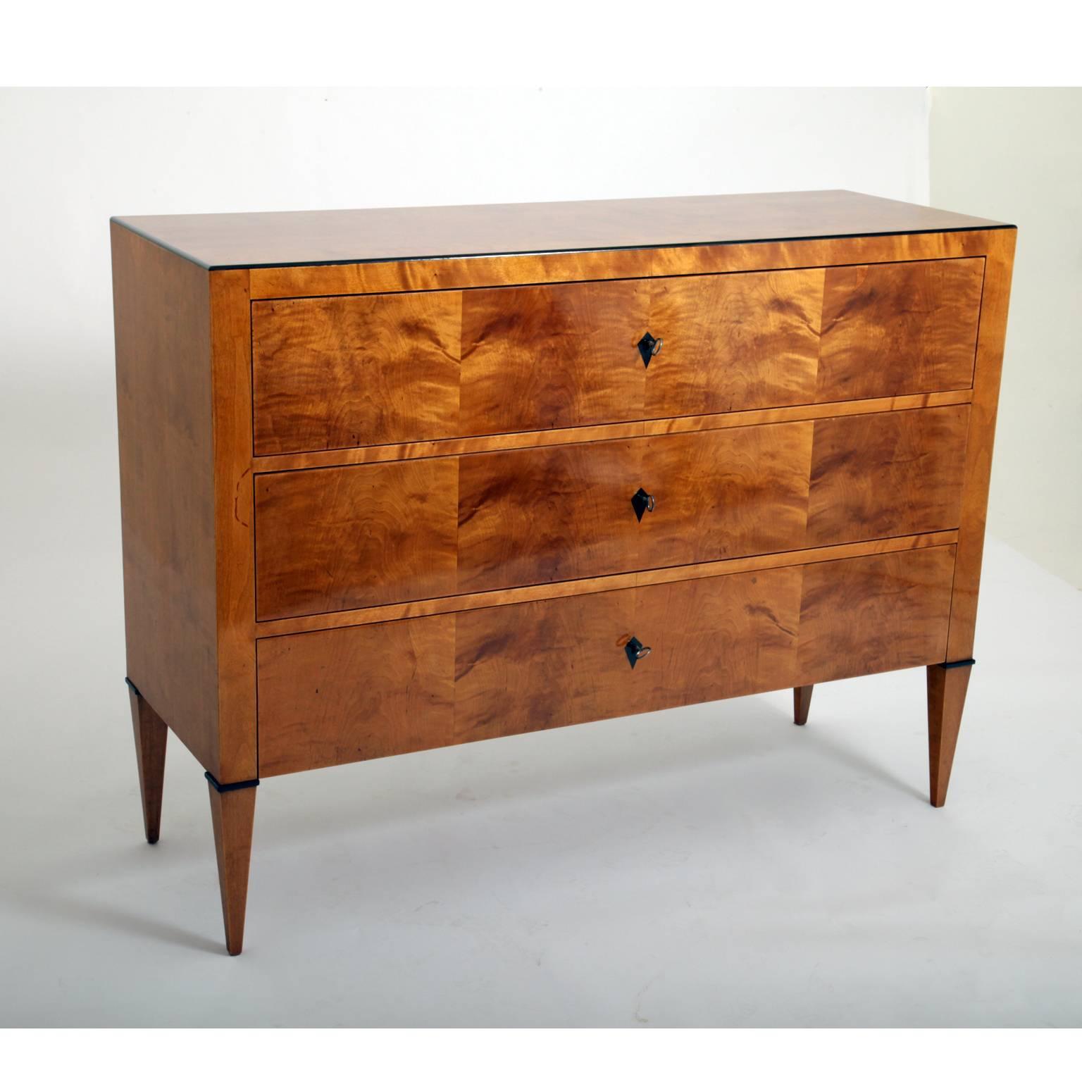 Biedermeier-style chest of drawers on tapered feet with ebonized details and rhomboid escutcheons. Smooth body with a black accentuated edge and a very beautiful birchwood veneer.