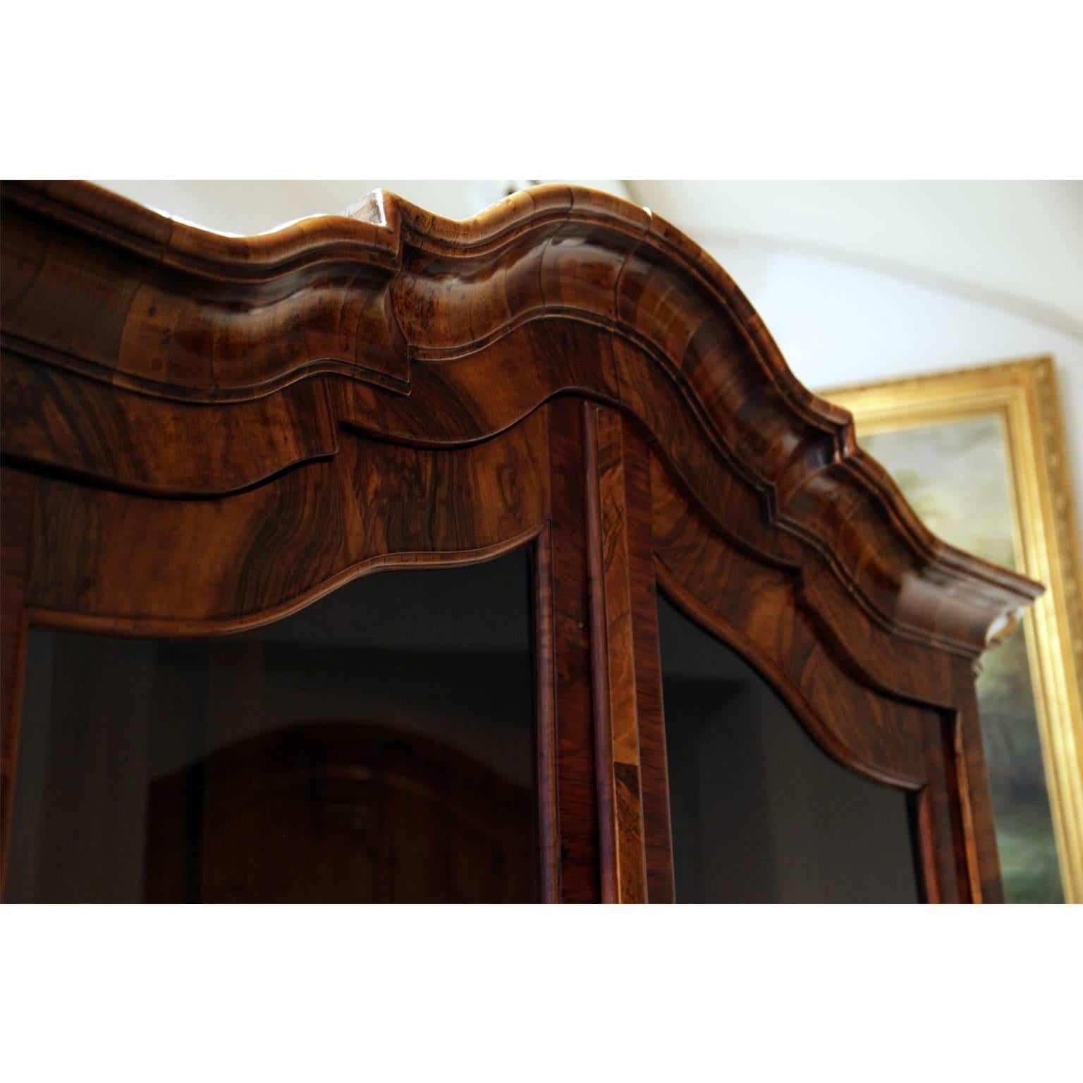 Baroque display cabinet with two doors and three-quarter glazing, as well as a curved pediment and rounded corners. Very beautiful walnut veneer. The feet are later.