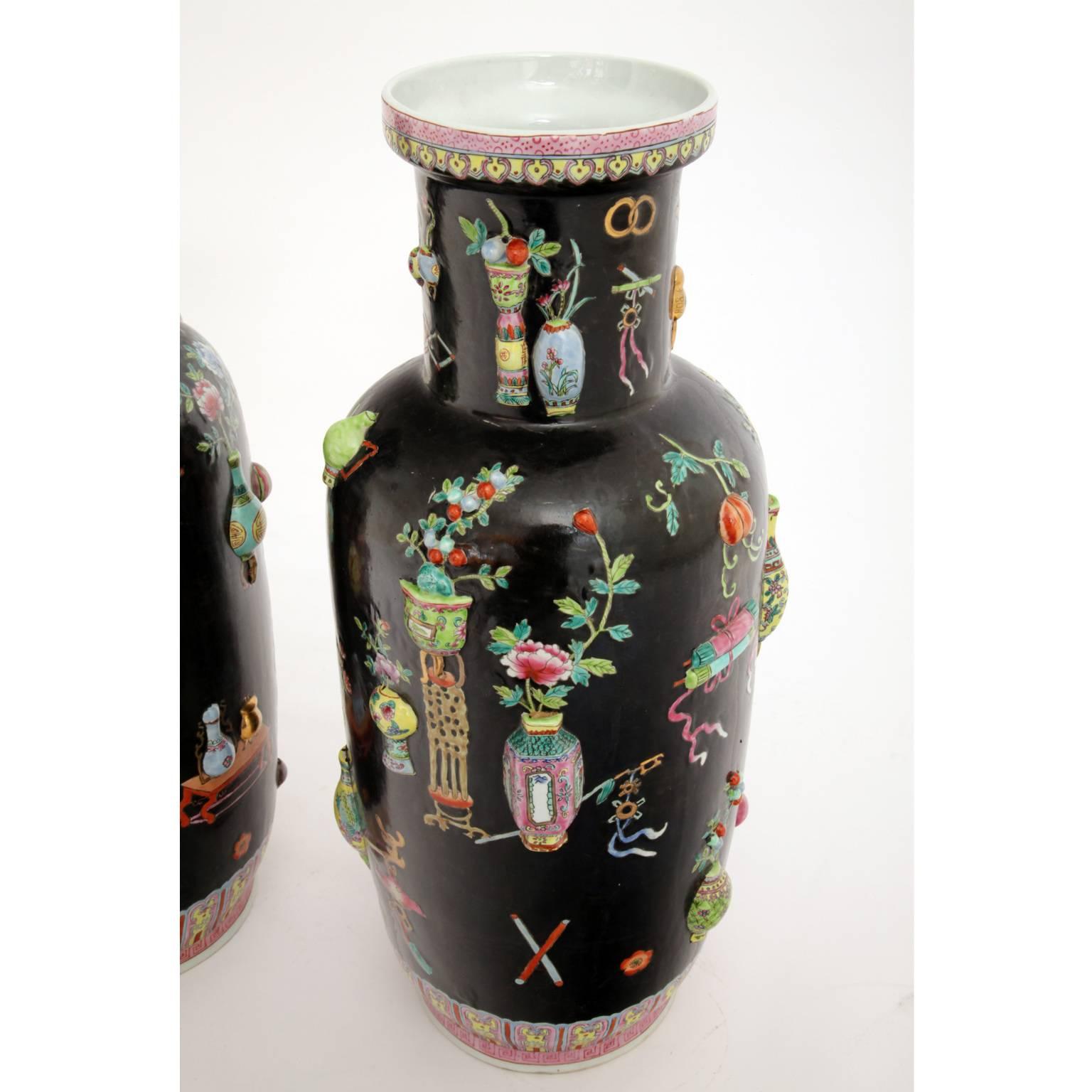 Pair of black Chinese porcelain vases with polychrome pictures of flowers and vases as well as good luck charms and symbols of eternity. Some of the depicted vases are three dimensional which gives the vases a very interesting and joyful look. There
