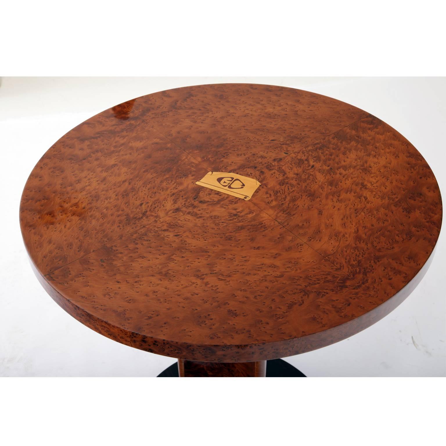 Art Deco side table on a round base with a trefoil stand and a round tabletop. The table is veneered with different woods. The different wooden grains give the table a very interesting and unusual look. The tabletop is inlaid with a GC as well.
