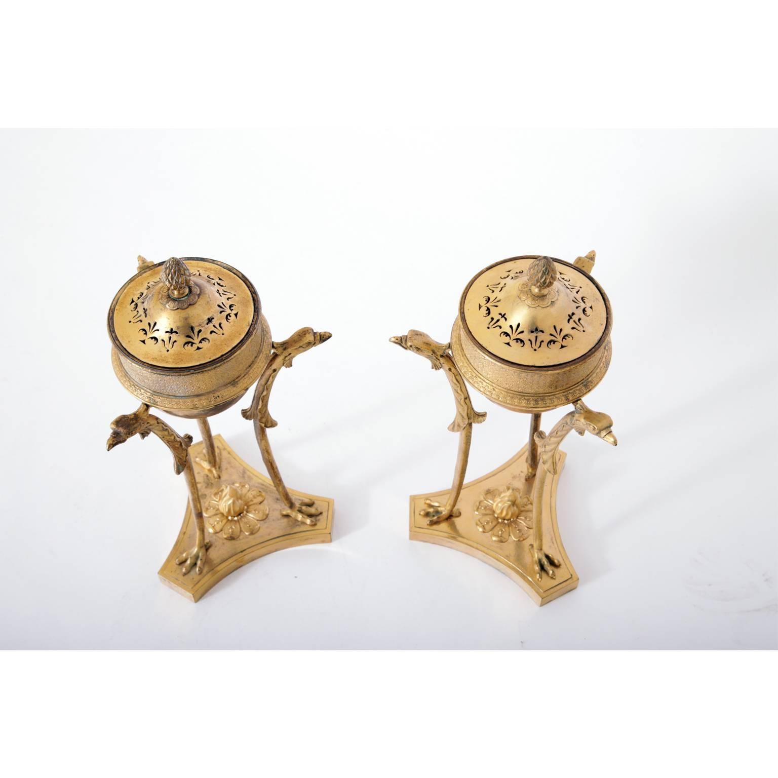 Pair of bronze tripod insense burners à la Athénienne on a trefoil Stand. The burner pot is held up by eagle-shaped legs with claw feet above a torchflame.
