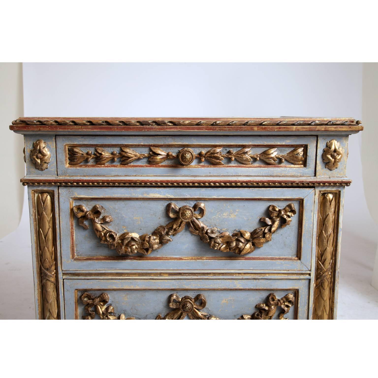 Three-drawered chest in Louis Seize style. Blue corpus with gilded carved festons on skirt, drawers and sides. The paint was professionally redone and has a slightly worn look to it.