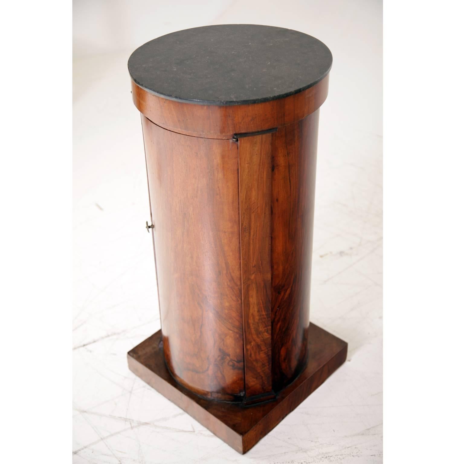 Cylinder-shaped cabinet on a square base with lateral pilasters with ebonized capitals. The top is black marble. The very beautiful cabinet is in an unrestored museum condition. The diameter of the top is 38 cm.