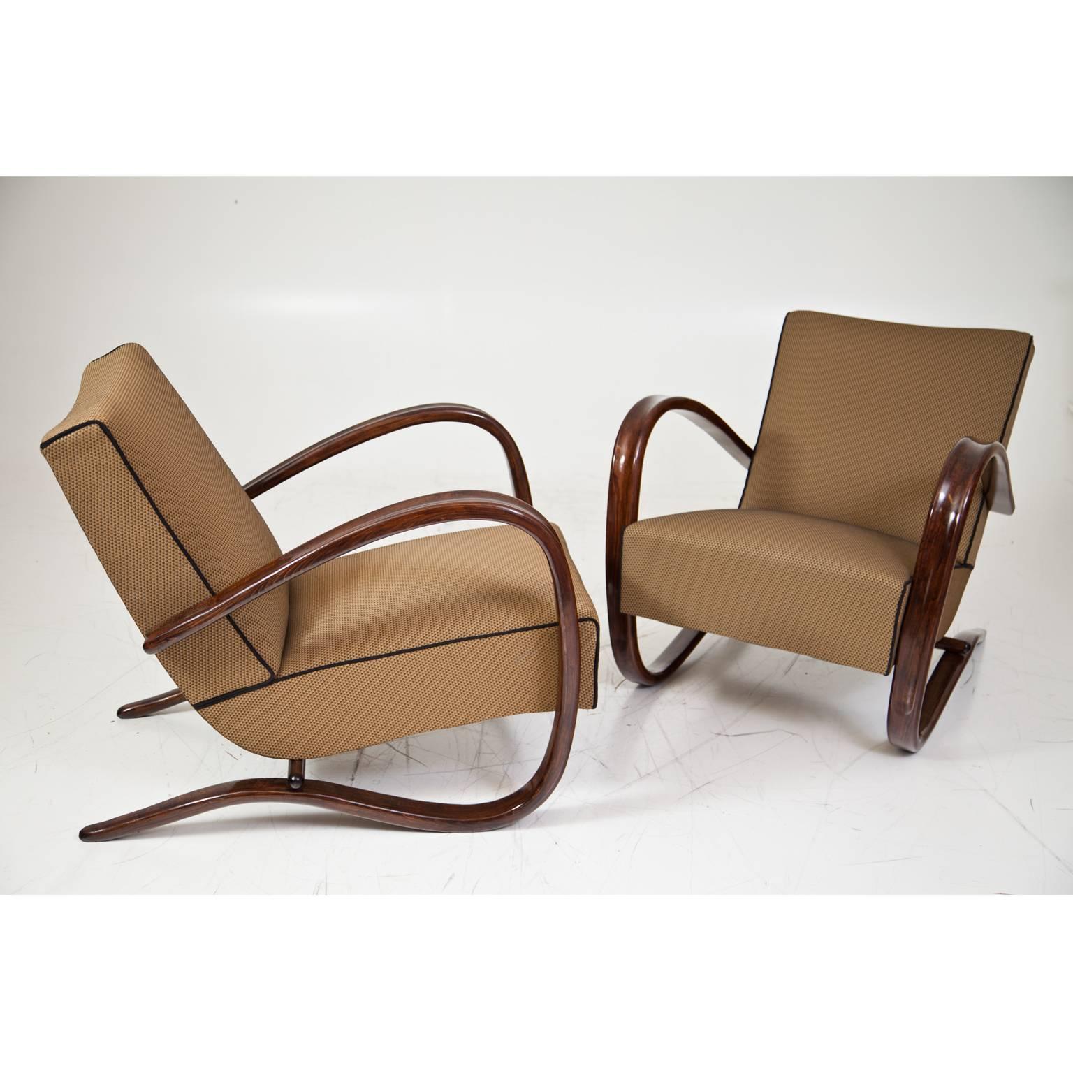 Iconic pair of chairs from the famous Czech designer Jindrich Halabala. The dark-stained armrests flow in an elegant c-shape around the side of the seating surface and become the frame of the chair. The chairs have been reupholstered.
   