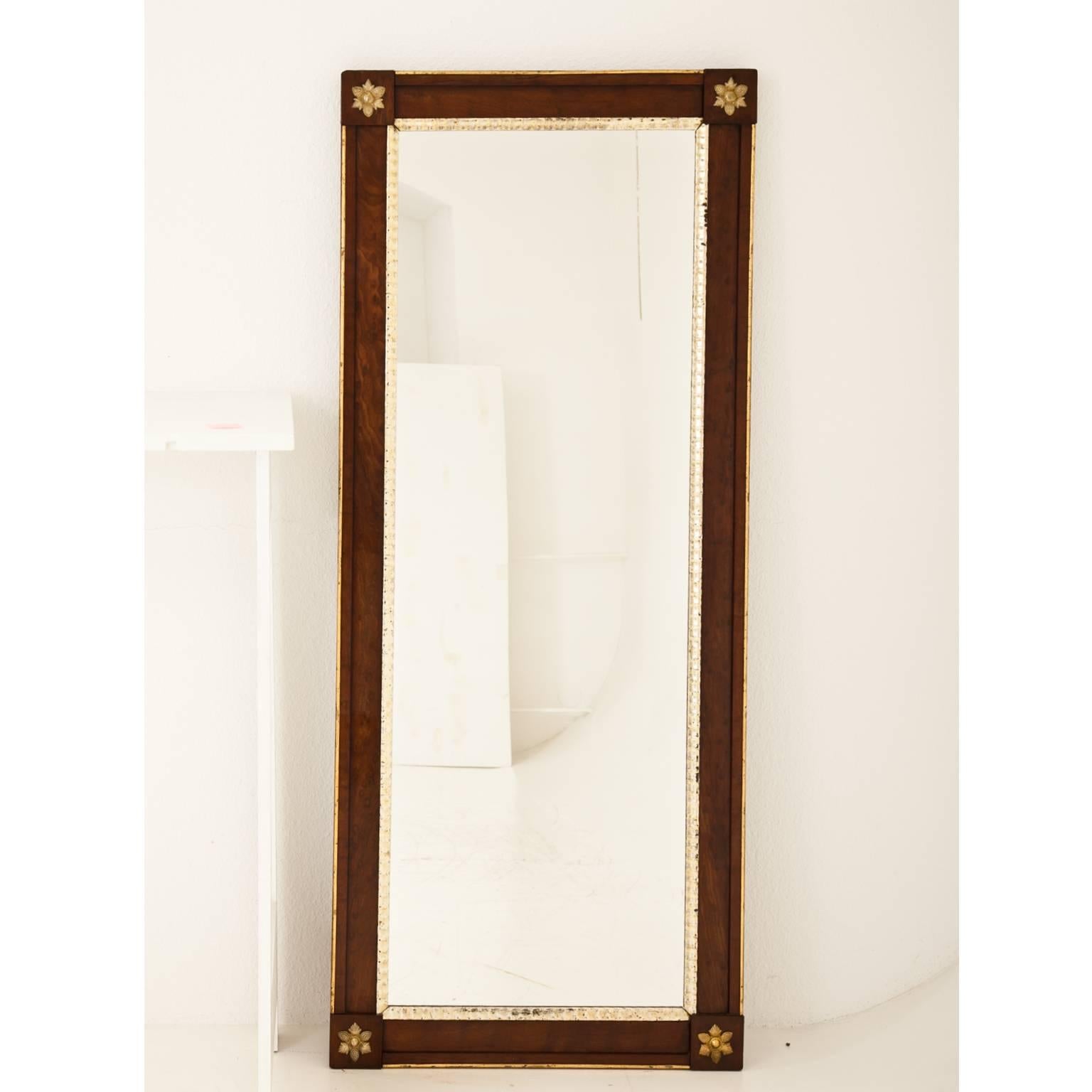 Large full-length wall mirror with brass trimmings and gilt moulding. Each corner is decorated with a brass flower. The measurements of the mirror pane are 147 x 50 cm.