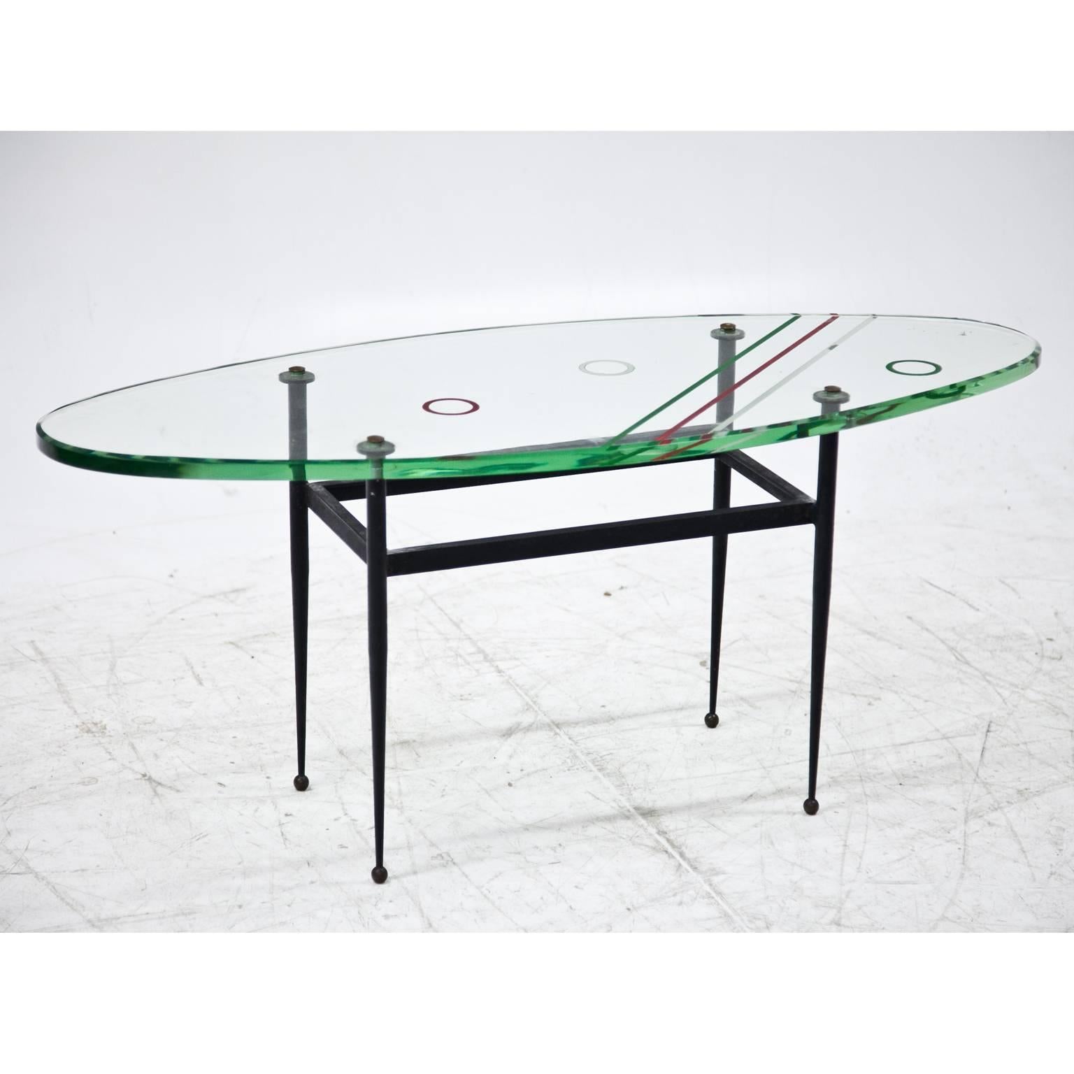 Italian coffee table on slender iron legs. The oval glasstop is painted with circles and lines in green, red and white.