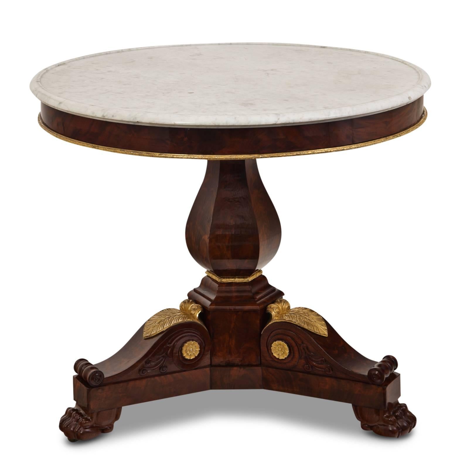 Elegant Empire Salon table on a trefoil base with lion's paws. Each foot consists of a large scroll with a gilt acanthus leave and flowers on each side. The round table top is white marble, the lower edge is decorated with a gilt brass strip.