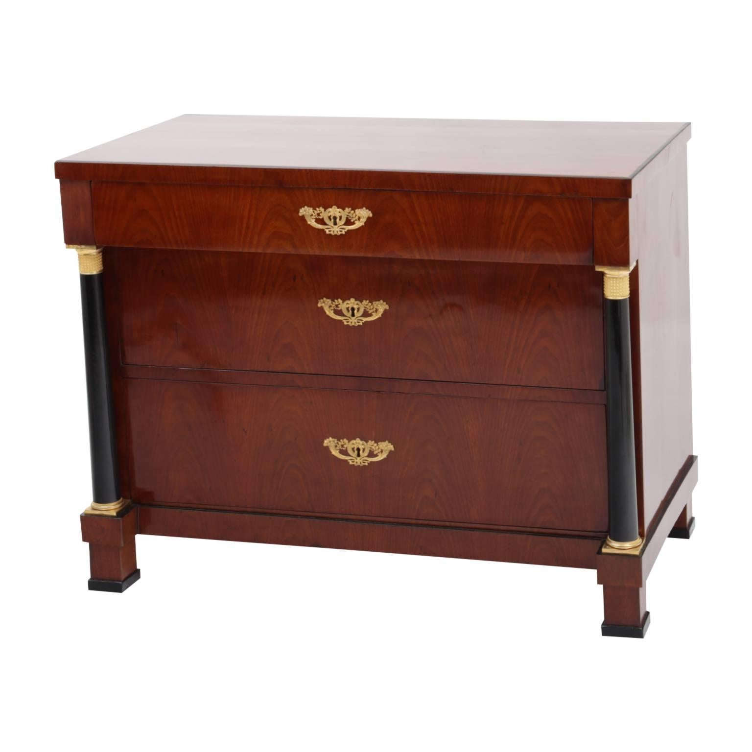 A pair of three-drawered Biedermeier chests with a mahogany veneer. Each of the dressers features two free-standing ebonized columns at each corner on the front of the pieces. The columns are topped with fire gilded capitals. The fittings were