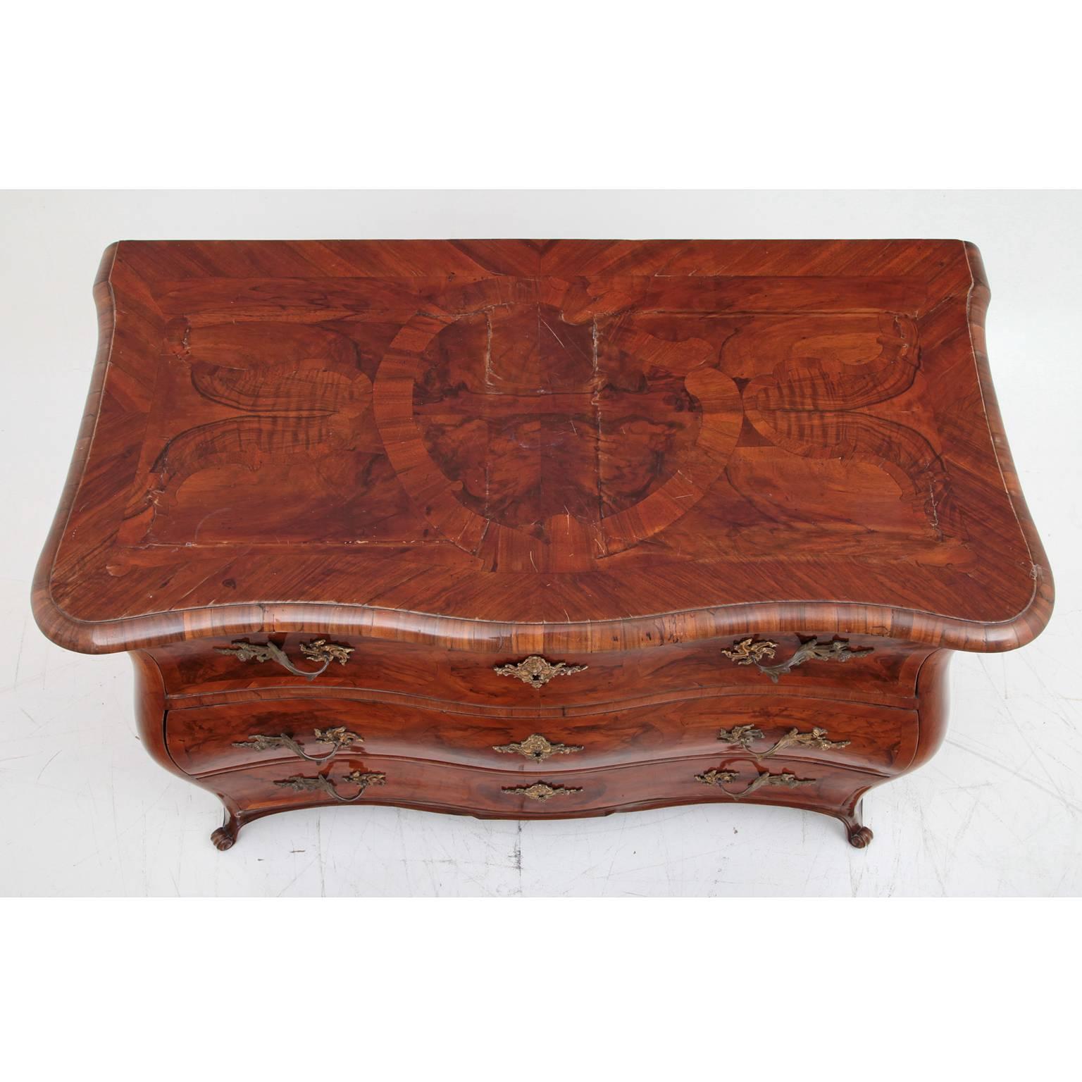 Baroque chest of drawers which stands on voluted feet and has three drawers with fire-gilded bronze hardware. The front and top of the piece are adorned with beautiful inlays.