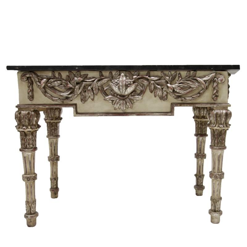 Exquisite Italian console table dating from the 1790s with black marble top and partly silvered legs and frame. The legs are fluted and slightly tapered, the frame is carved with beautiful leaf-ornaments. The black marble top was replaced.
