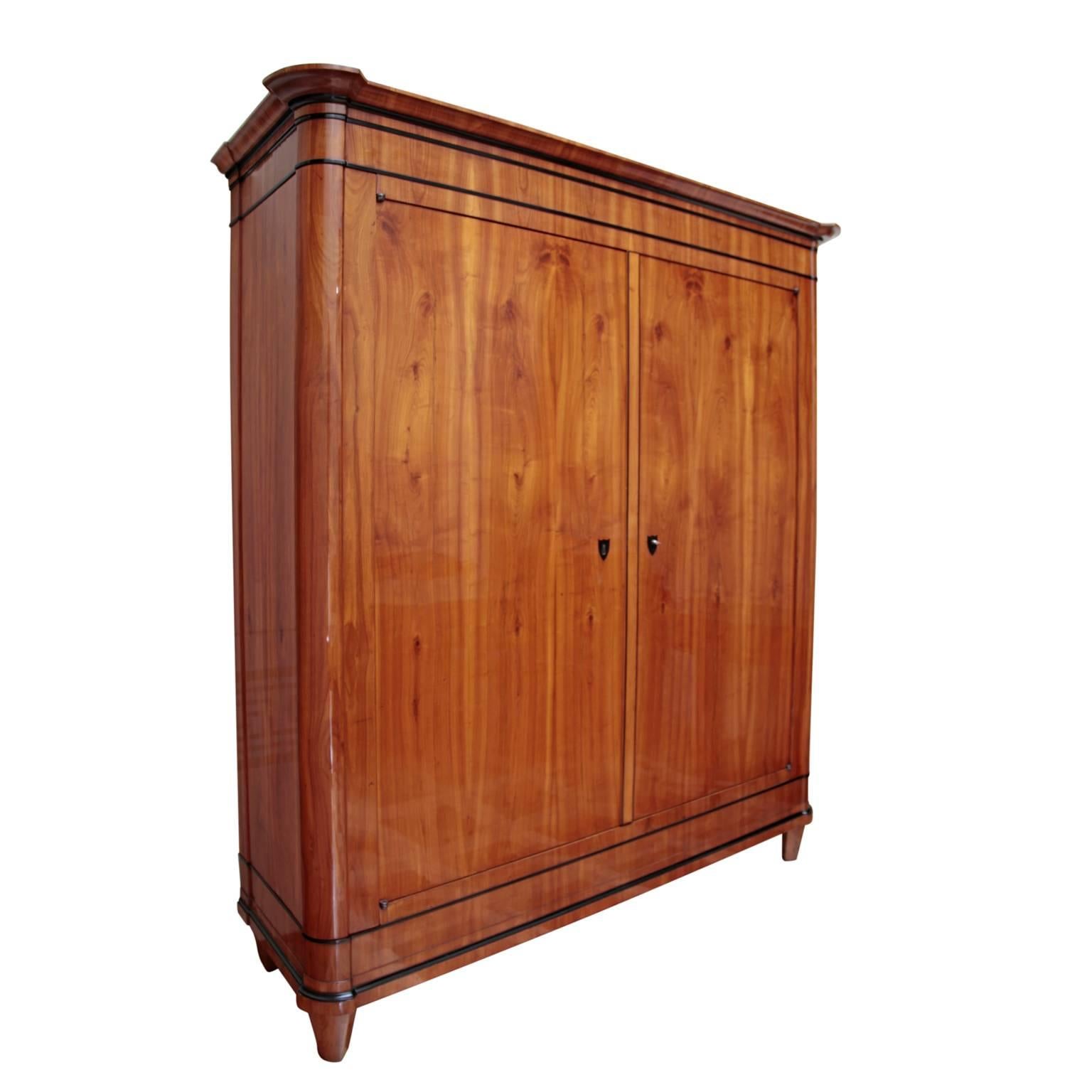 Large wardrobe standing on tapered feet, prob. from Munich. The wardrobe has two doors and rounded corners. The top part and the base frame are profiled and slightly protruding. The cabinet is decorated with ebonized mouldings and escutcheons. On