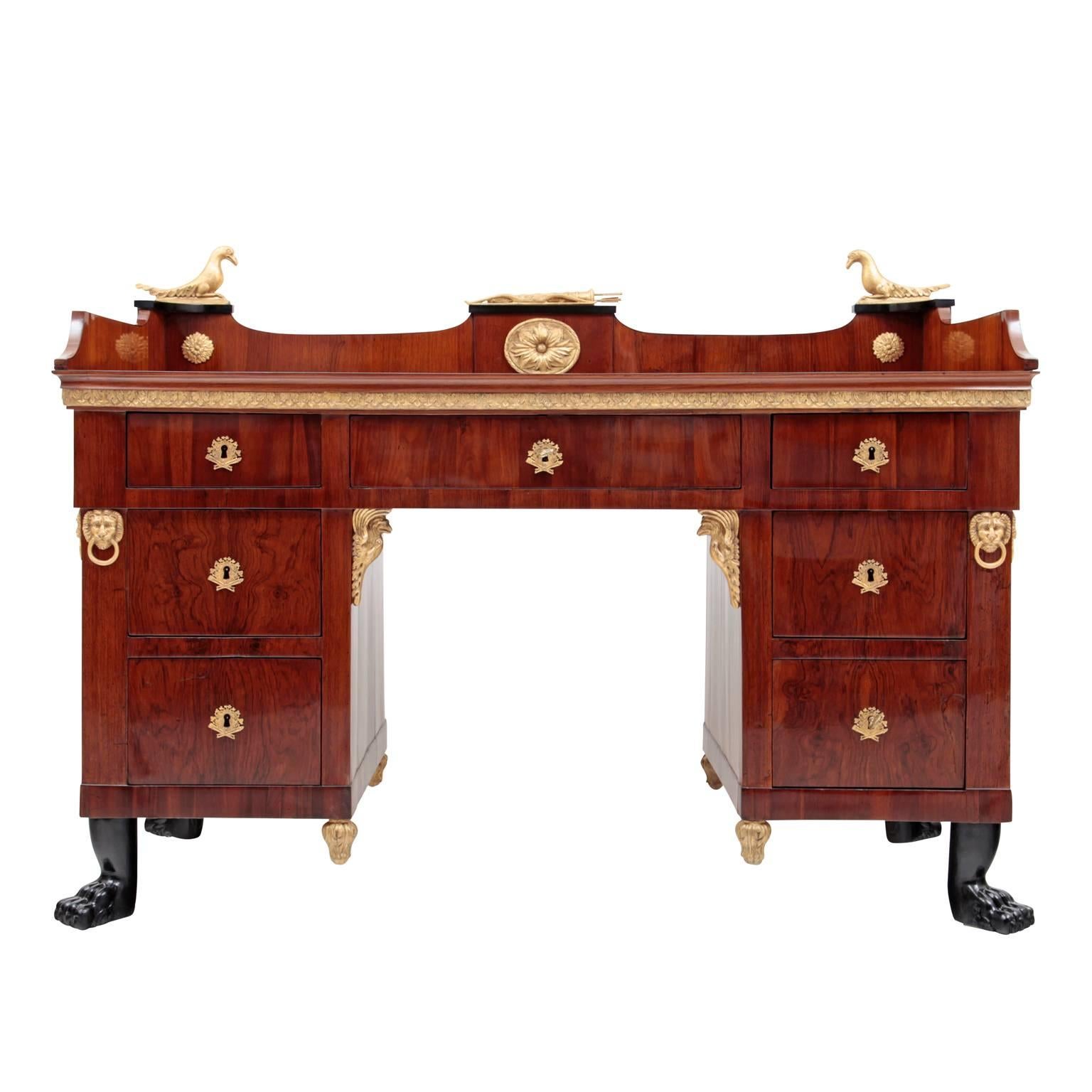 The writing desk probably comes from the Baltic States, stands on lion's feet and has a beautiful red colored walnut veneer. On the left and on the right side are three drawers, with a broader drawer in the middle. Inside the middle drawer is a