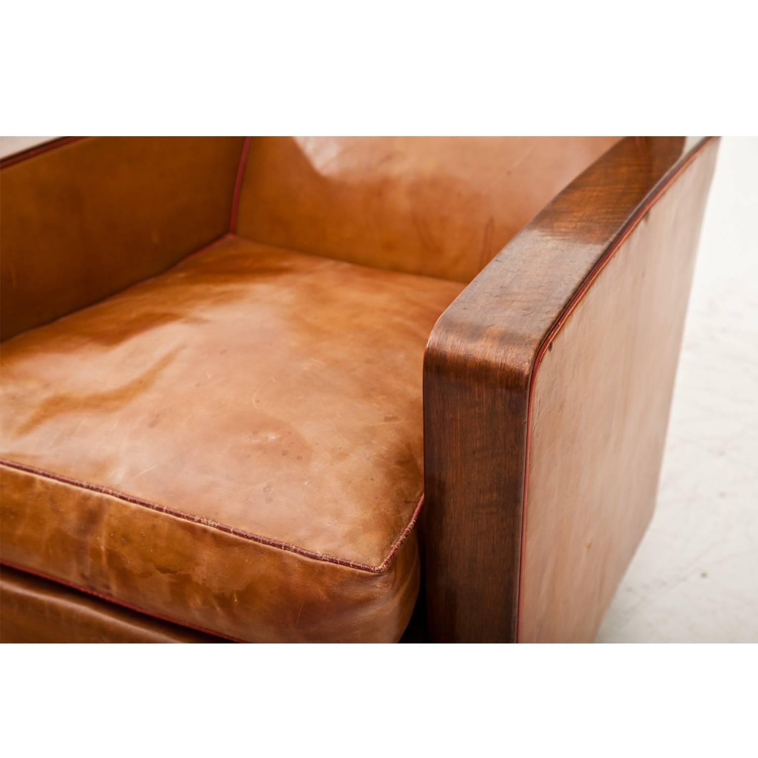 Comfortable Art Deco armchair on an unusual stand. The armchair is covered with a Cognac-colored leather with red trimming. The leather shows decorative signs of age and use.