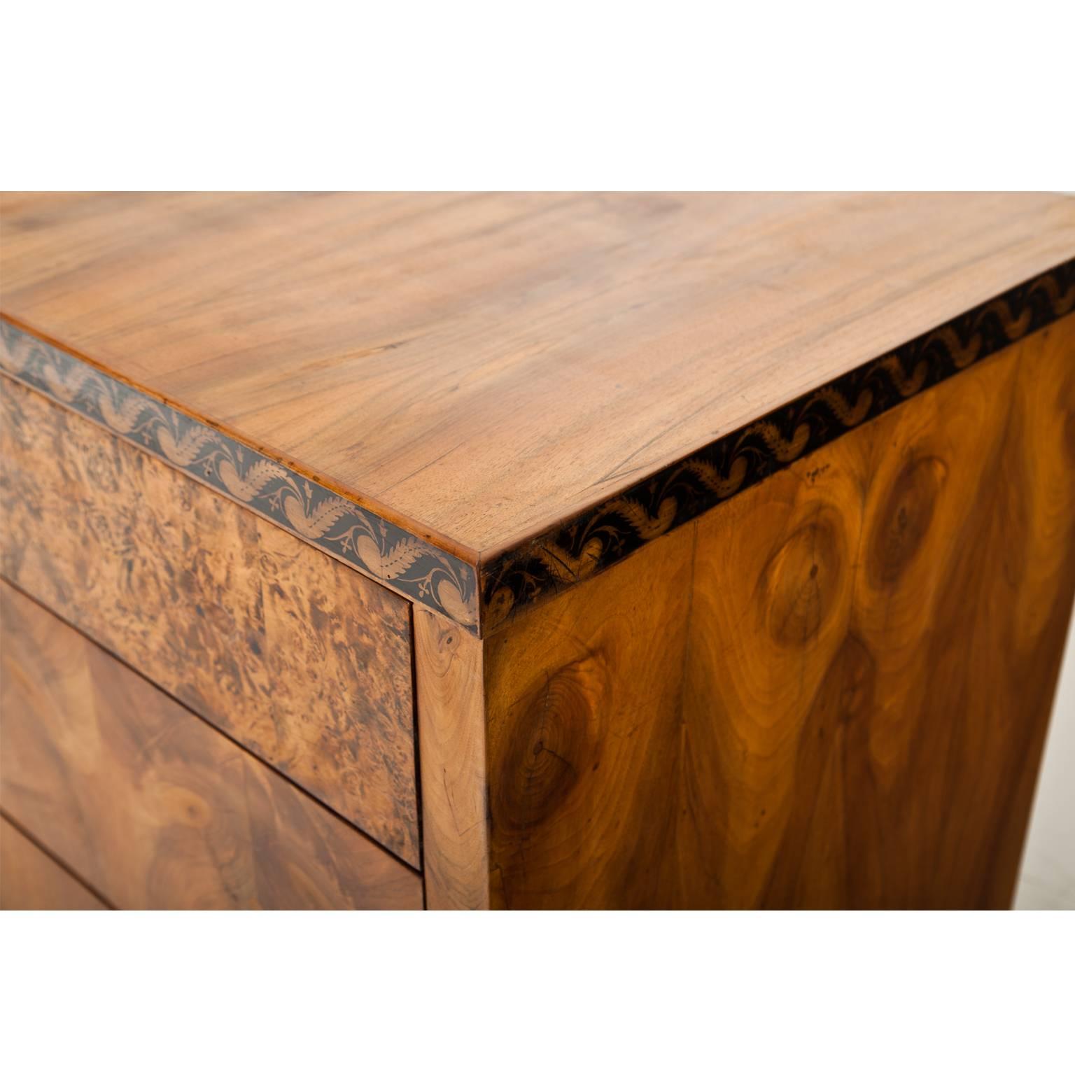 Three-drawered Biedermeier chest of drawers on tapered feet. The chests has a beautiful walnut veneer pattern and a revolving black ink ornament at the top edge.