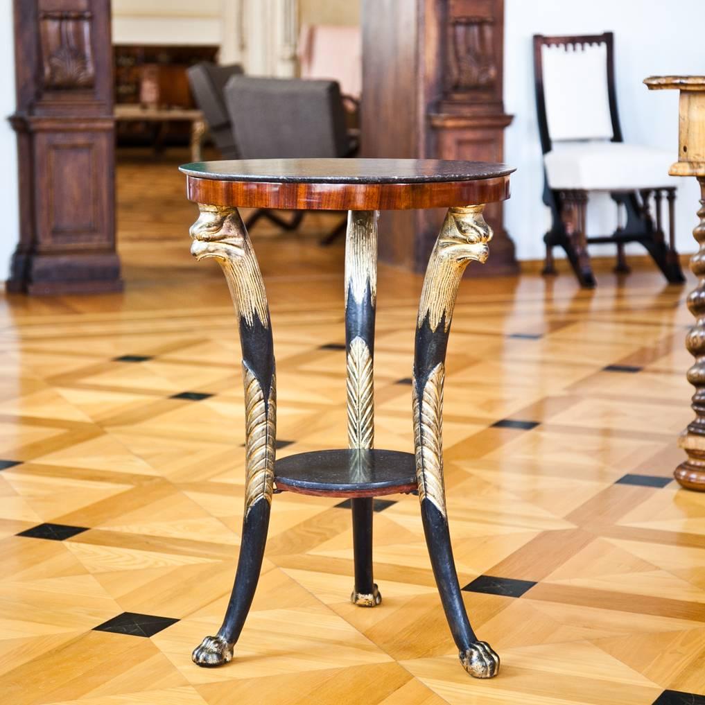 The very decorative and beautiful table is supported by three carved and partly gilt legs with eagle heads and claw feet. They hold a circular marble shelf as well as the marble top in the same style. The top has an old, hardly visible crack.