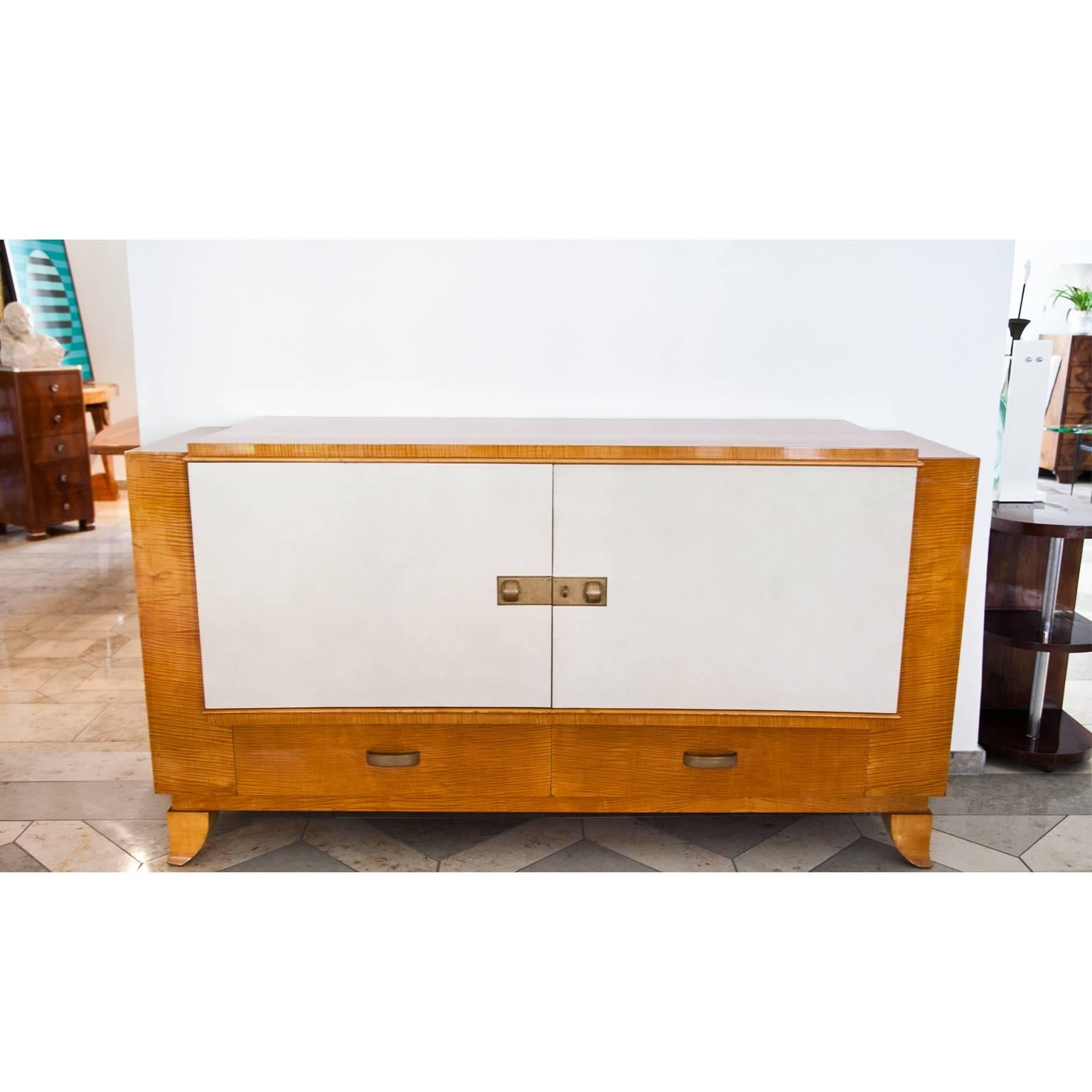 Art Deco sideboard on curved feet with two drawers and a middle compartment with two doors. These are covered in a light colored faux leather.