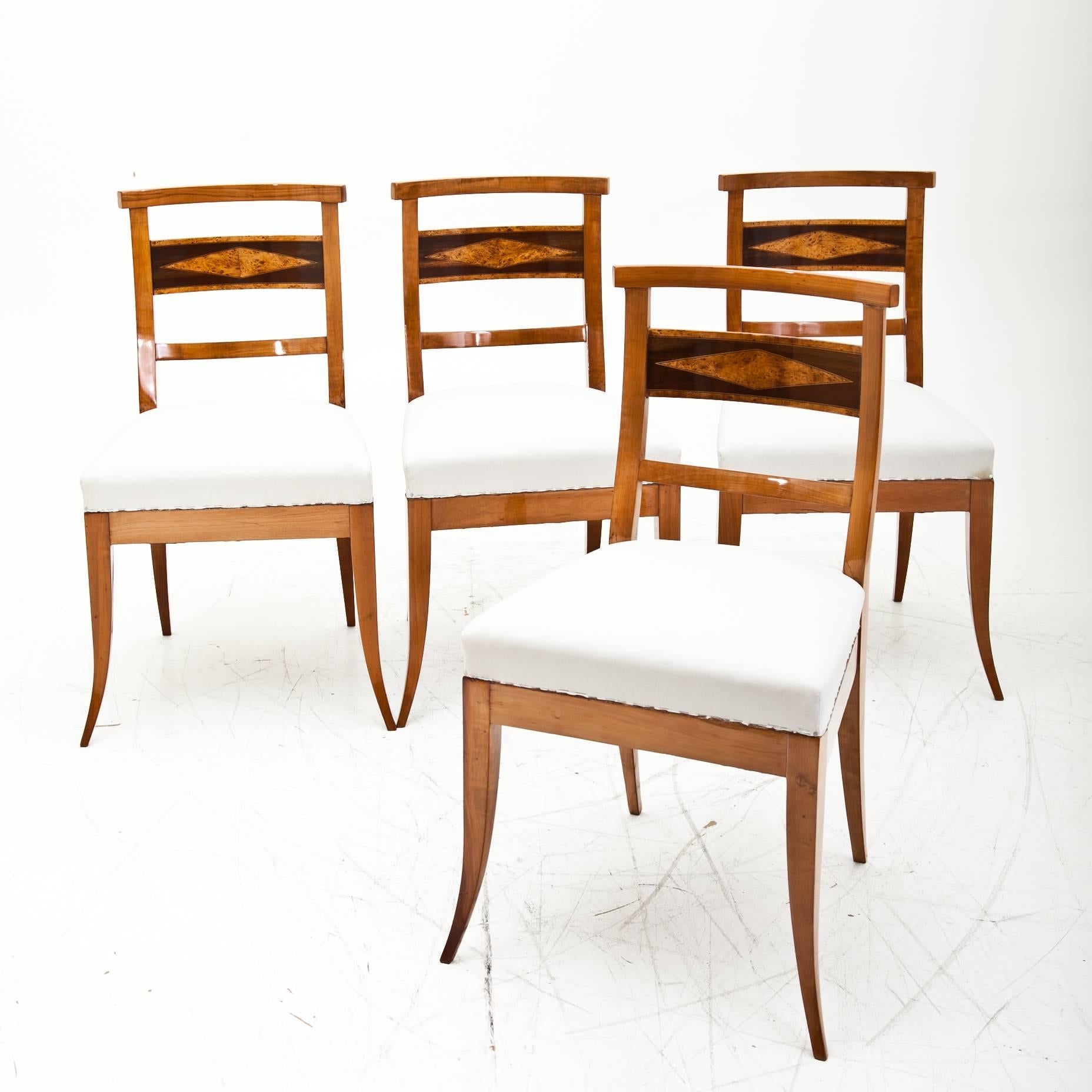 Four Biedermeier dining room chairs on elegant curved legs. The backrests are decorated with a rhomboid burl wood veneer.