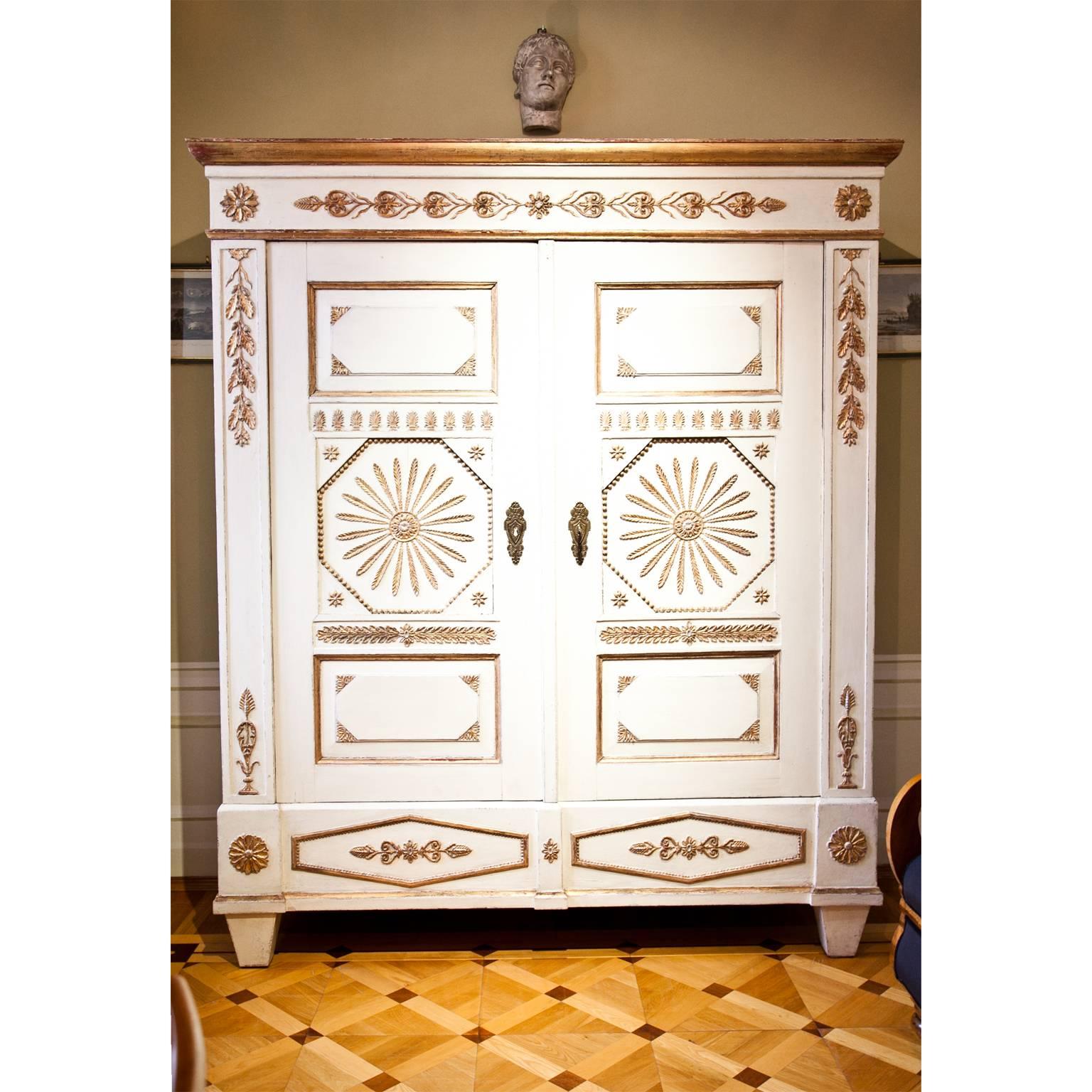 Two-door cabinet with gilt ornaments on a crème-colored base. The interior is fitted with a coat rack and shelves to the right, making it a perfect wardrobe.