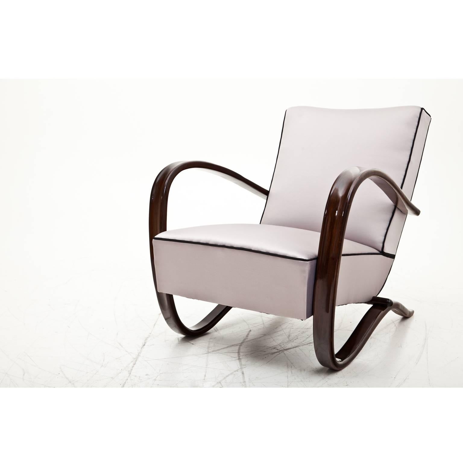 Iconic pair of chairs from the famous Czech designer Jindrich Halabala. The dark-stained armrests flow in an elegant c-shape around the side of the seating surface and become the frame of the chair. The chairs have been reupholstered with a very