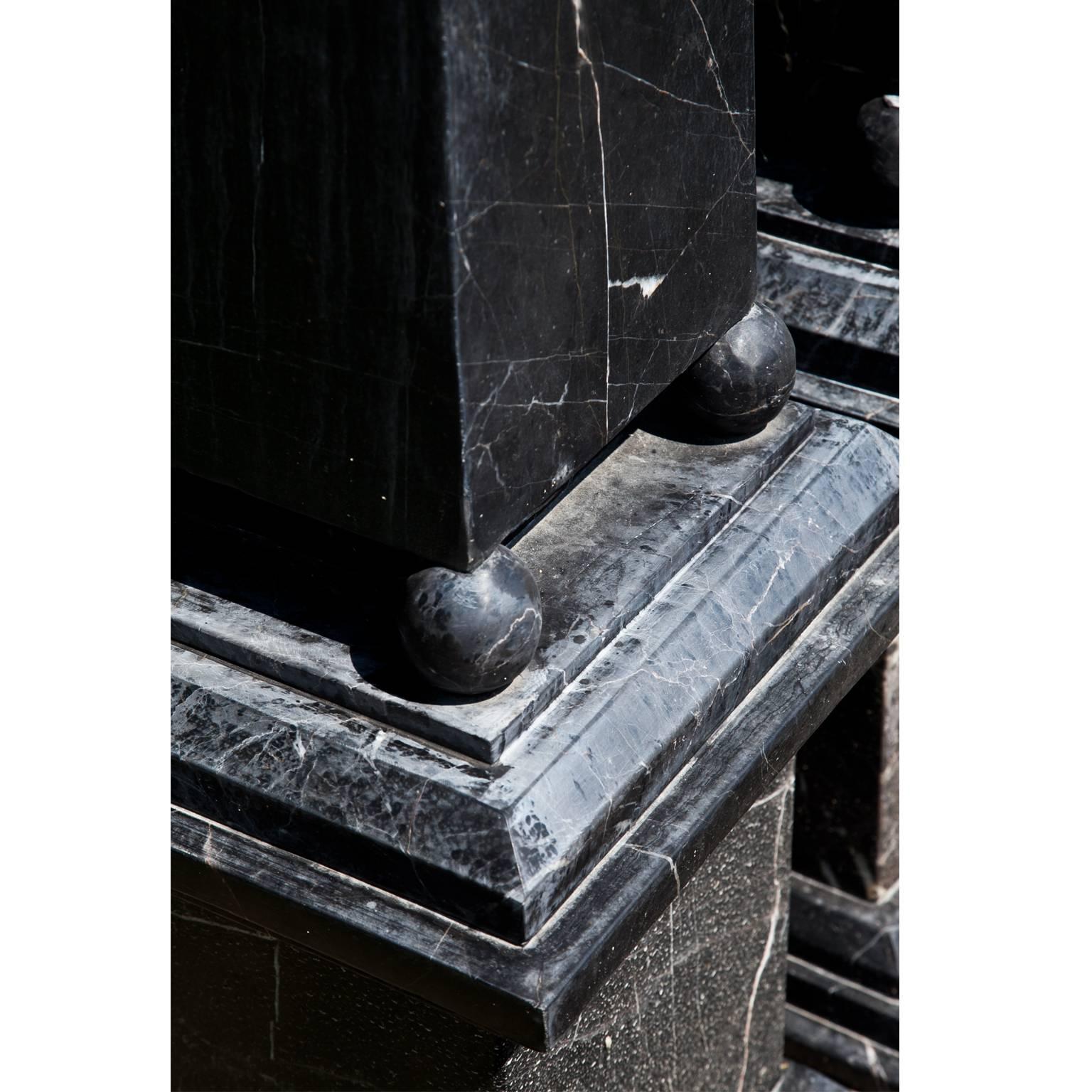 Pair of obelisks out of black marble with white veins. The obelisks stand on spheres above square bases. One sphere is missing.