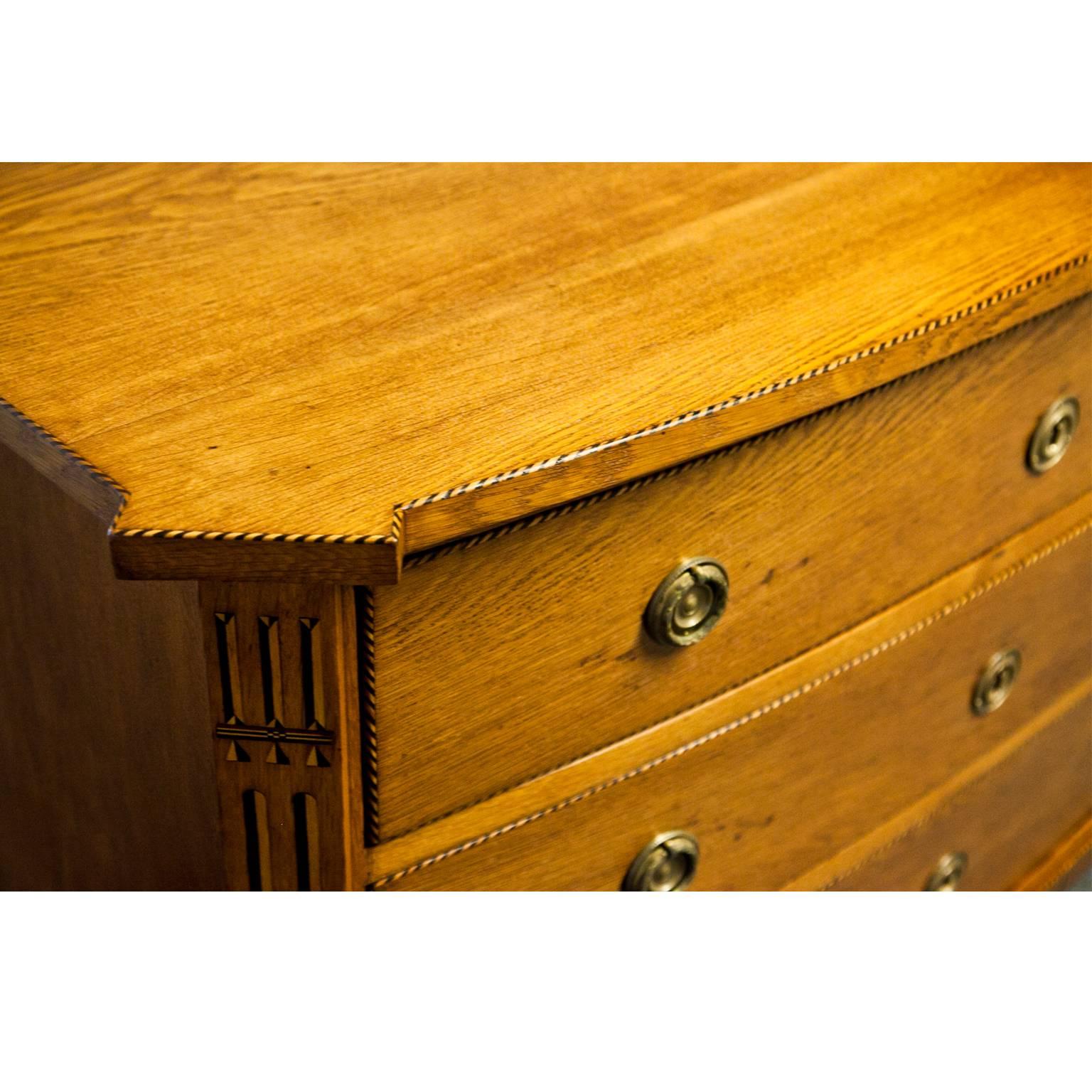 Three-drawer chest of drawers with slightly curved front, standing on tapered feet. The slanted corners as well as the skirt and the edges are decorated with filet marquetry.