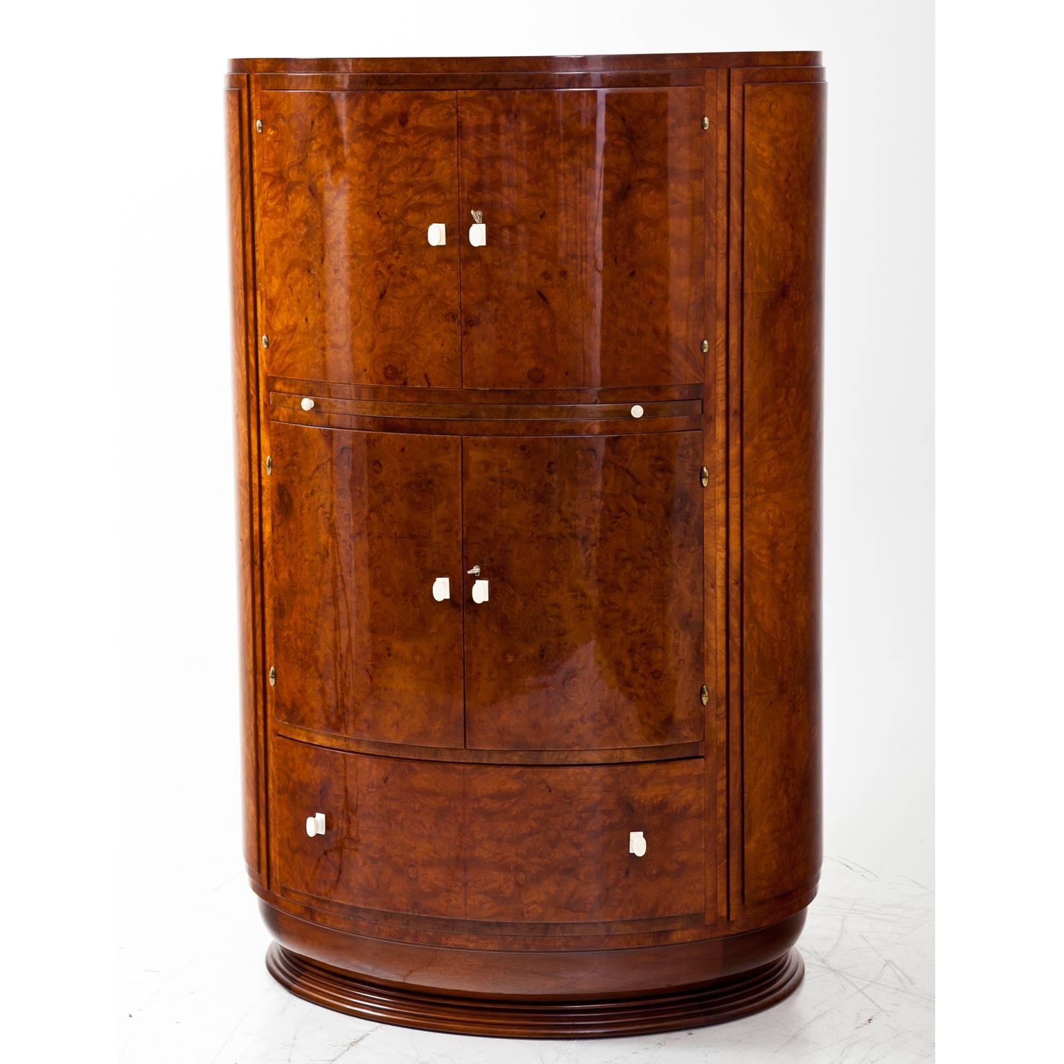 Art Deco bar cabinet with an oval body on a profiled base. The handles are bone and the sides are accentuated. The cabinet has at the bottom one large drawer, the middle and the top are two-doored compartments for bottles and glasses.