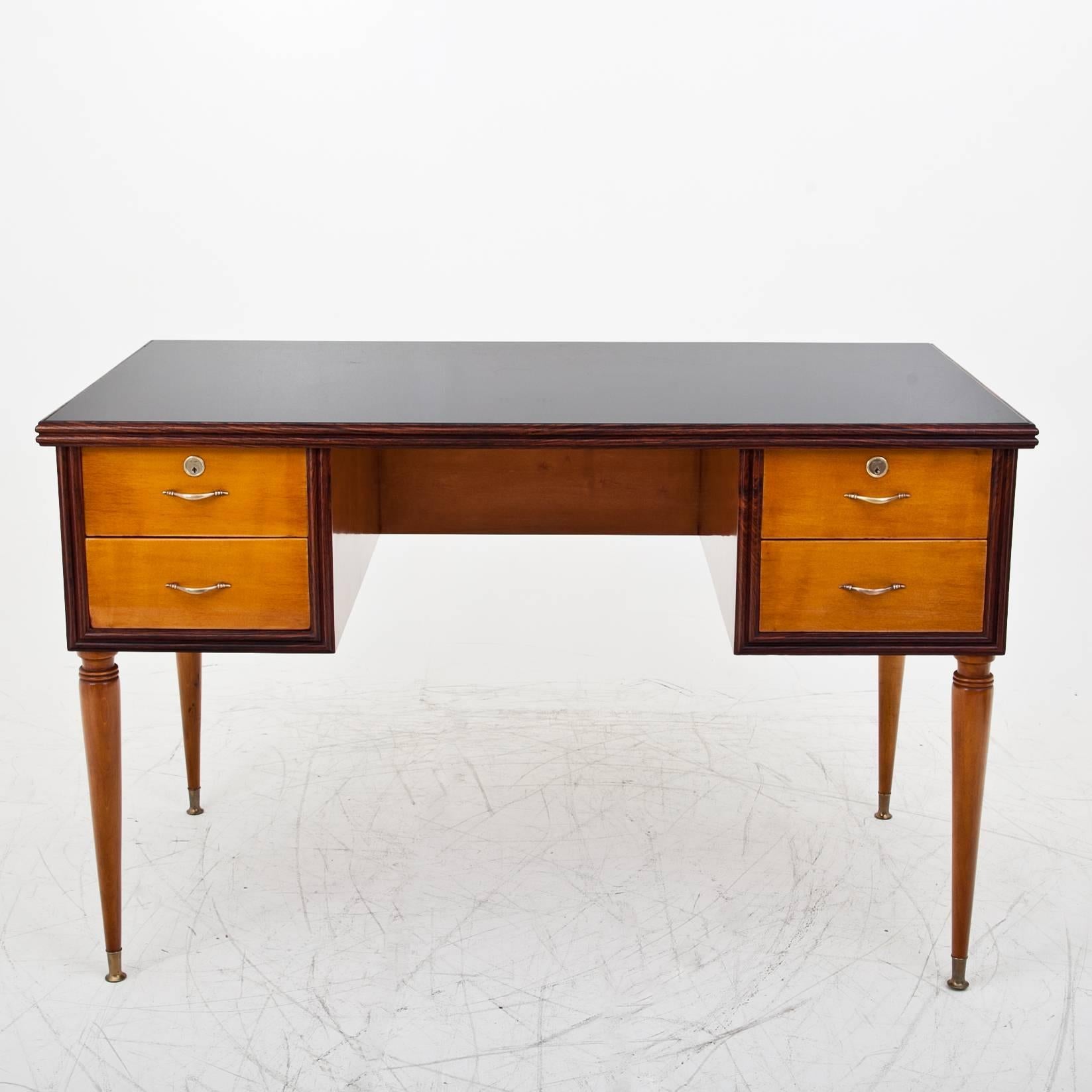 Italian desk, standing on conical legs, with four drawers and a stained glass top. The writing surface and the drawers are framed by a darker colored wooden edge. The table is designed for an all-round view and in a professionally restored condition.