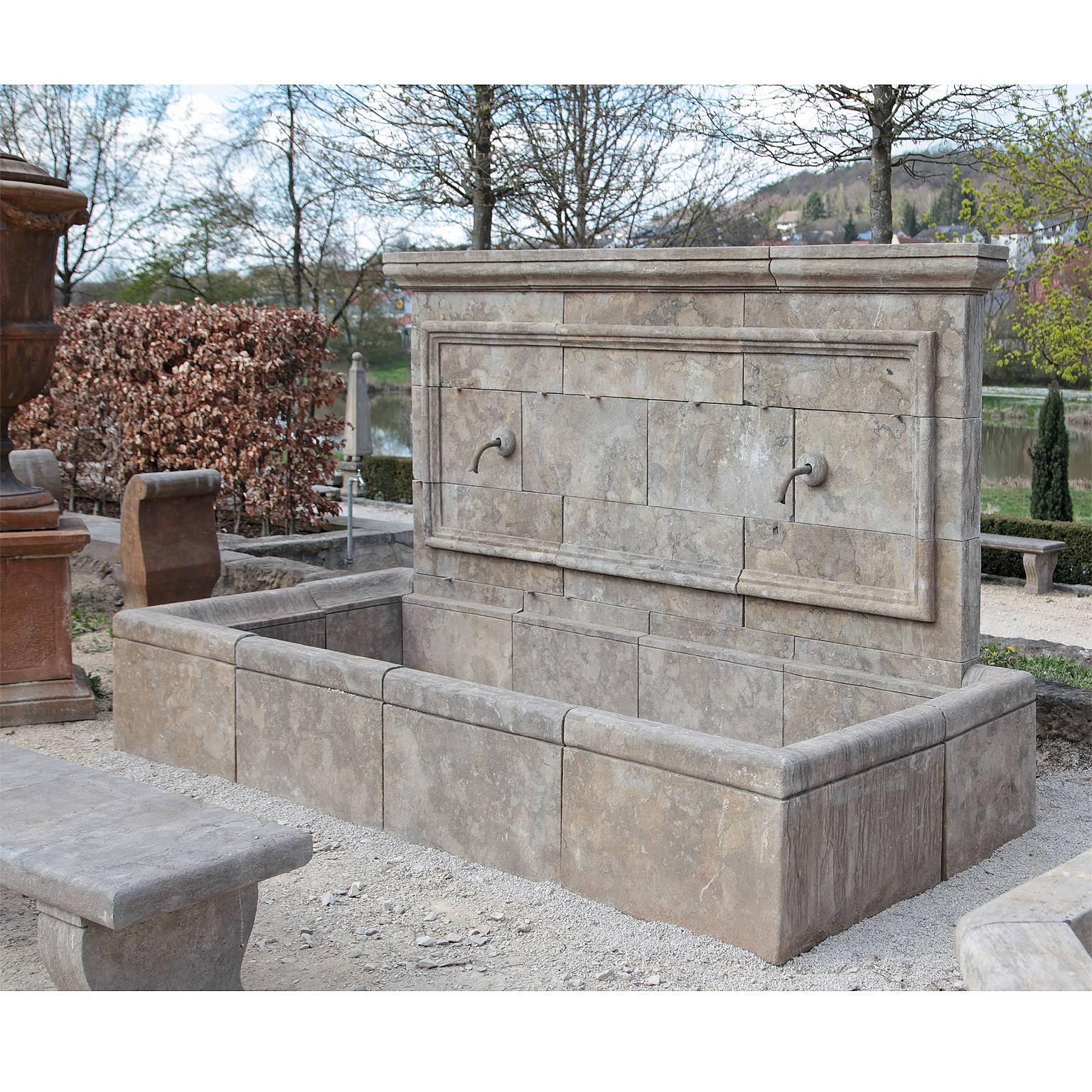 A large wall fountain made from blue stone with a rectangular basin. The back wall is architecturally divided and features two spigots. The height of the basin is 50cm.