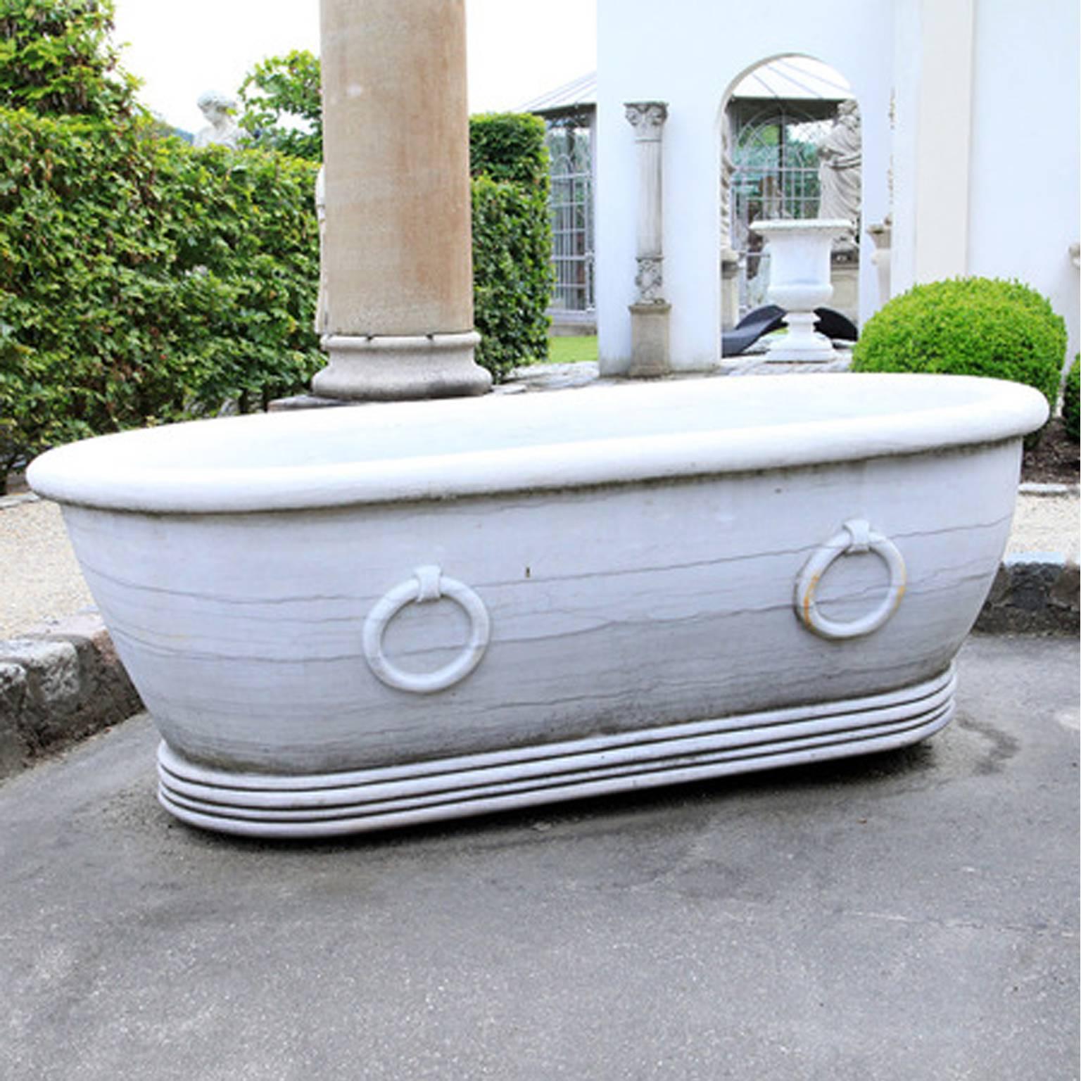 Oval bath tub with stylized rings on the wall and profiled stand, out of marble and designed for the garden.