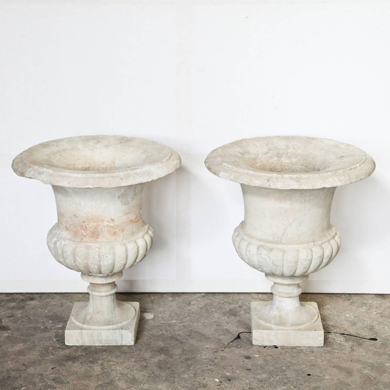 Pair of off-white Italian marble vases on baluster-shaped feet above square bases. The lower third of the vase shows a bellied, gadrooned wall. The vases have old restorations, the bases were added later.