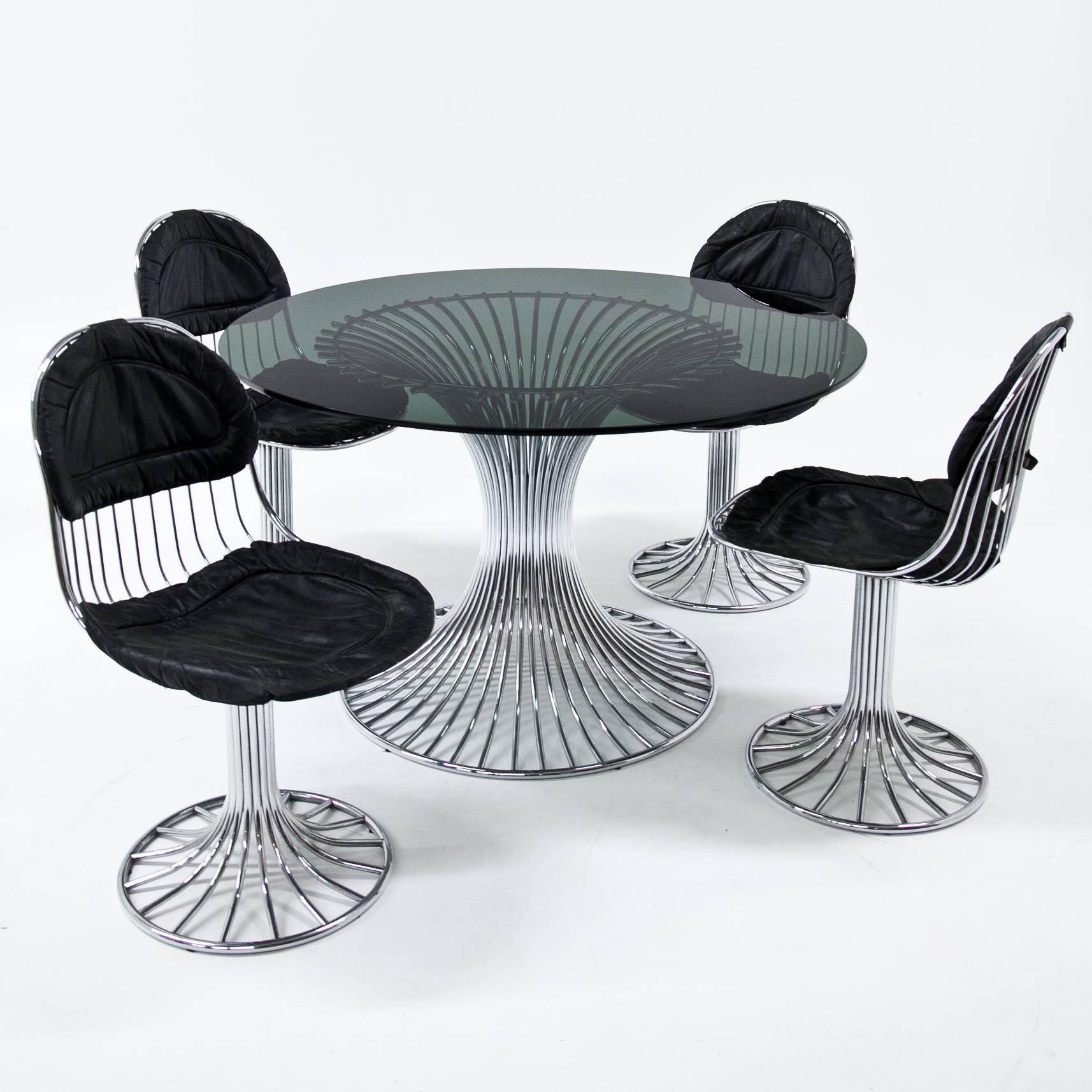Modern dining room ensemble consisting of one table and four chairs in the style of Warren Platner. The table has a chromed metal tubular base and a circular smoked glass top. The chairs in a similar design, are upholstered with black leather
