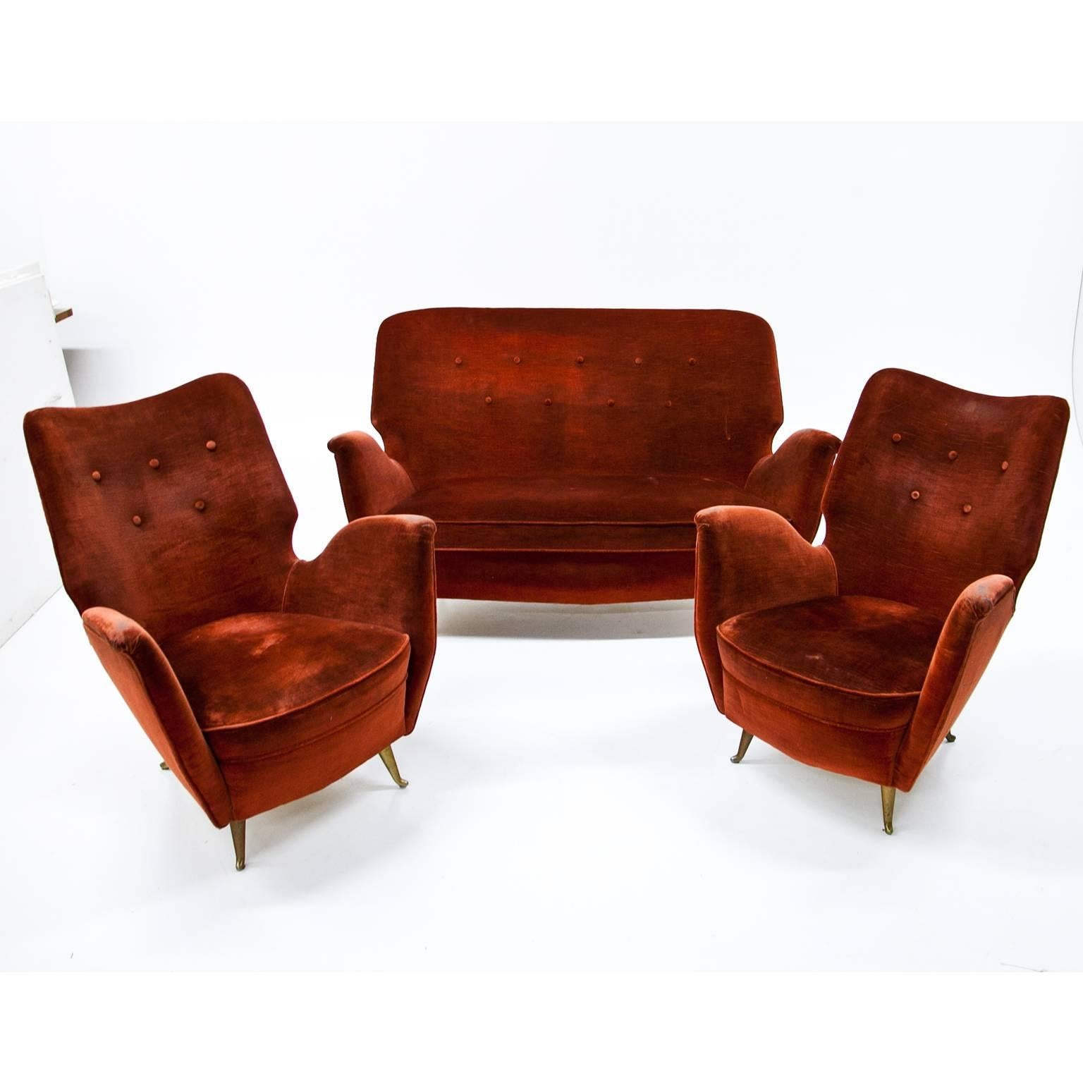 Seating ensemble consisting of a two-seat sofa and two lounge chairs on tapered brass feet. The group is in an absolutely original condition. The red fabric shows some signs of wear, the basic upholstery is in a good condition. Length of Sofa: 135