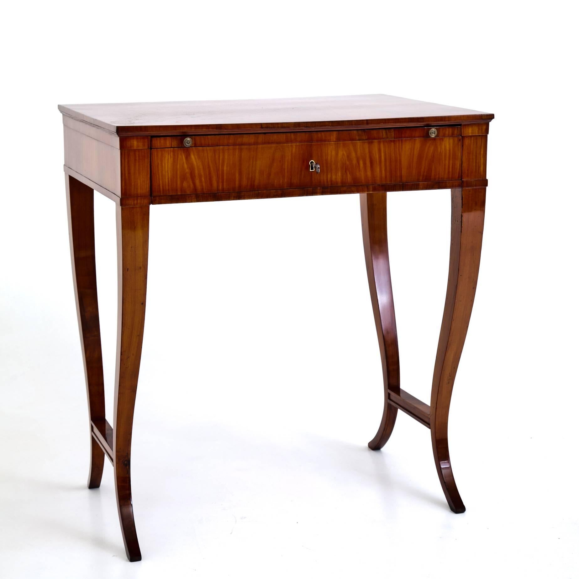Elegant Biedermeier writing table out of cherrywood, standing on curved legs with connecting stretchers. The large drawer has three more small drawers towards the back. Above is a pull-out writing surface, covered with black leather.