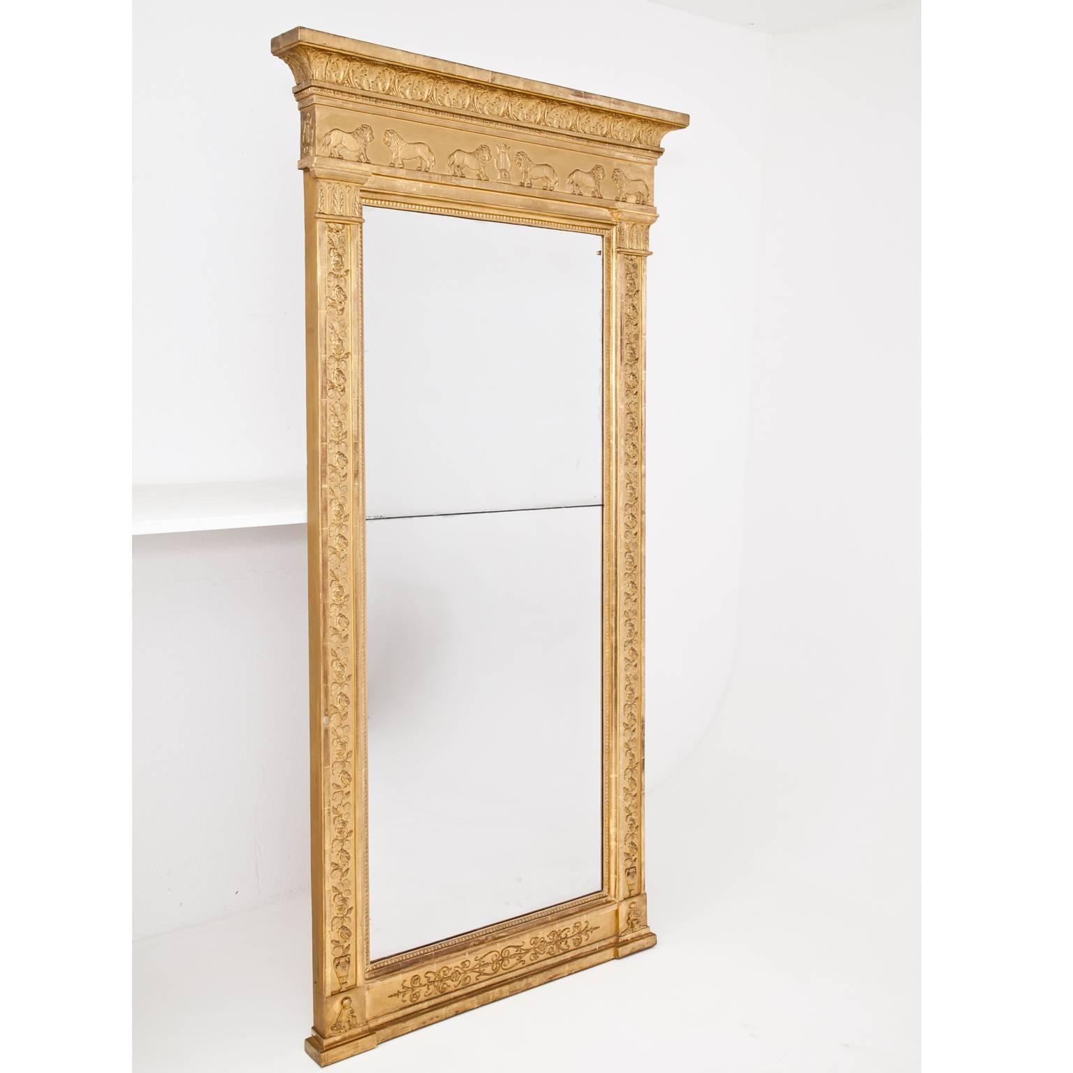 Large neoclassical wall mirror in a gilt wooden frame, decorated with rose-garlands, capitals and pacing lions as well as small cupids with fruit baskets and flutes. Gilding is original, the old mirror is divided in the middle. Mirror size: 157 x 66