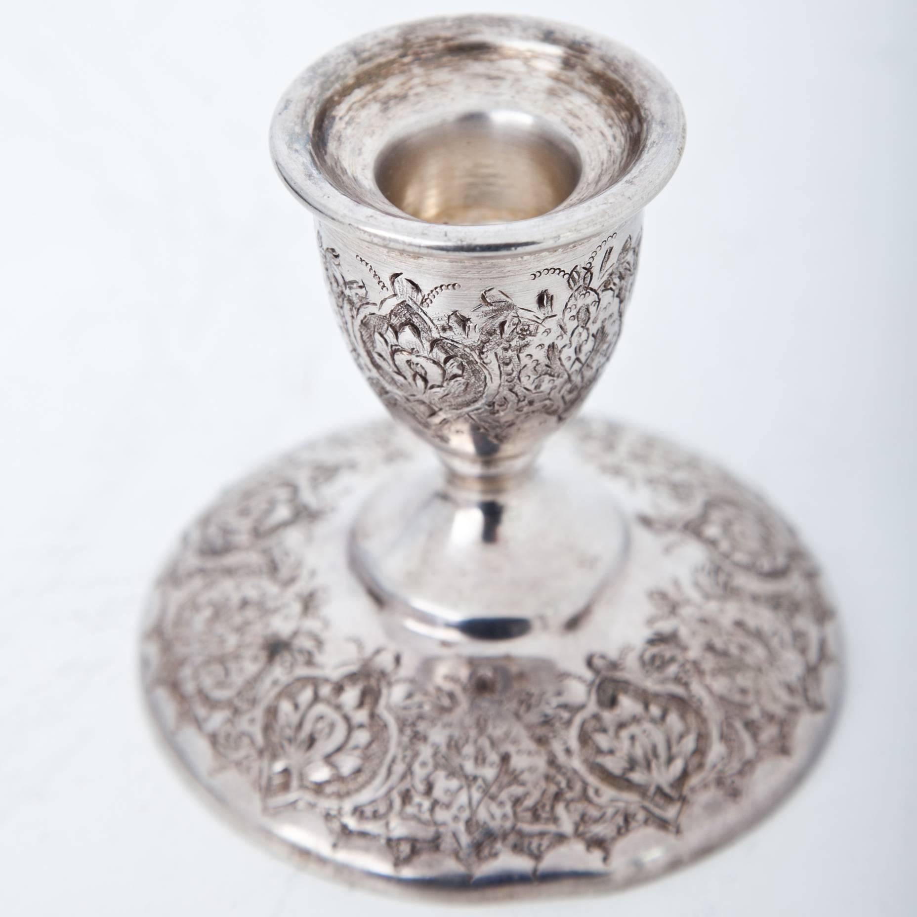 Small silver candlestick on a round foot with baluster-shaped shaft and tulip-shaped spout. The candleholder is decorated with carved flower and leaf ornaments. Illegible embossed at the foot.