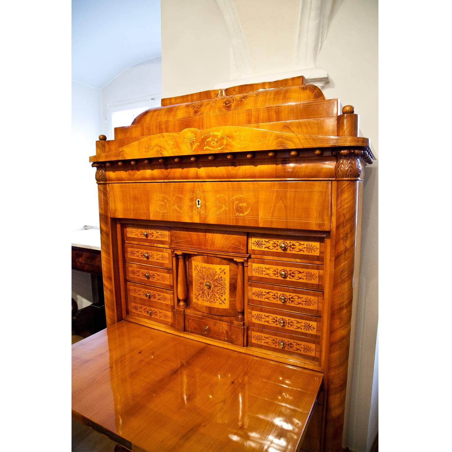 Cherrywood Biedermeier Secretaire with a three-drawer chests of drawers base and a lockable top drawer. The stepped pediment with revolving ball-frieze hides another drawer. Three-quarter columns with carved leaf-capitals flank the secretaire, which
